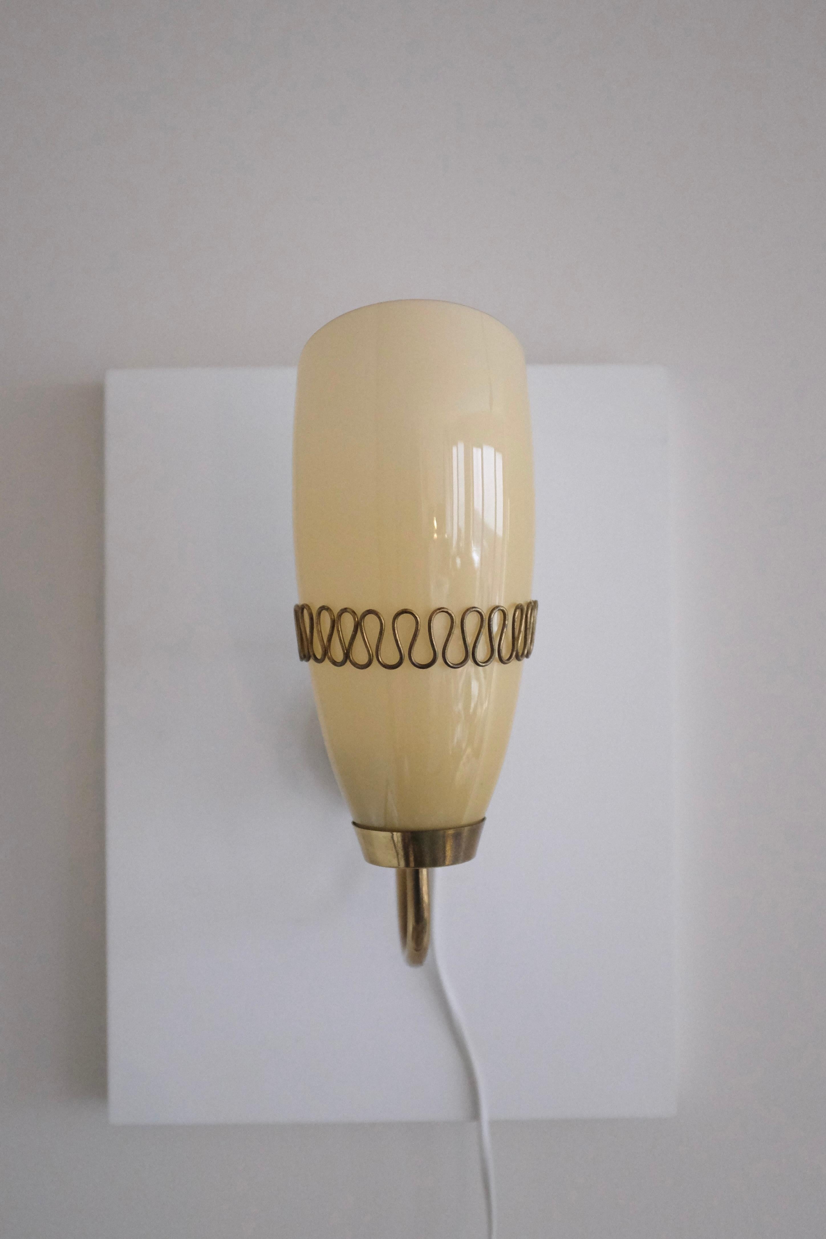 Beautiful Mid-Century Glass and Brass Wall light by Mauri Almari for Idman, Finland. Brass lamp arm with a filigree design that wraps around the oval shaped glass lantern in a beige color shade. Age appropriate wear to the brass with patina and two