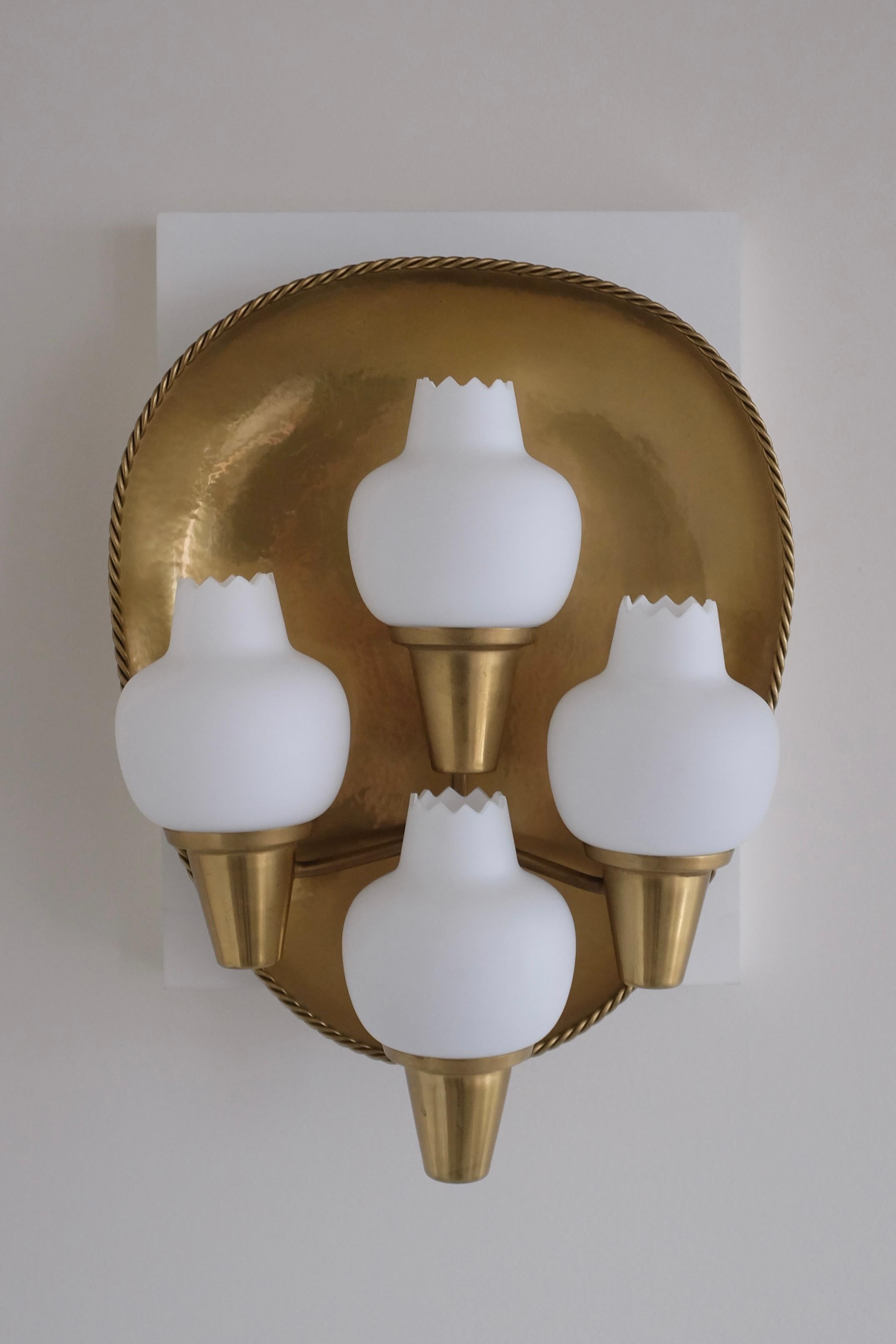 Stunning and rare wall scone in model 405 by Ateljé Lyktan, Sweden. A large brass back with a beautiful twisted pattern around the border holds 4 lamp arms each with a white opaline glas lantern. Produced around the 1940/50s and possible designed by