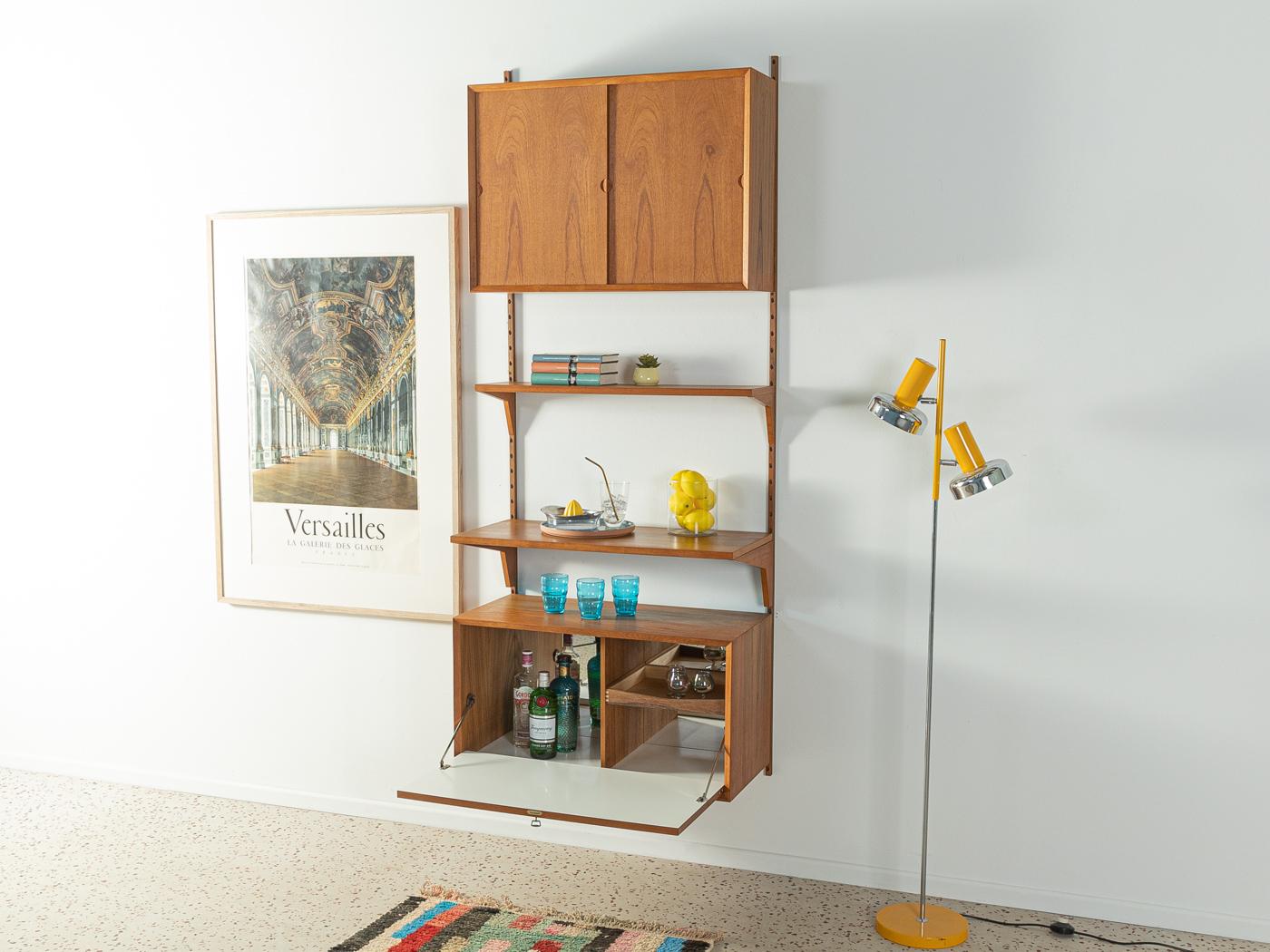 Classic shelving system from the 1960s, the high-quality containers and shelves are veneered in teak. The system consists of two shelves, a container with sliding doors, a bar container with folding door and two wooden ladders.

Quality