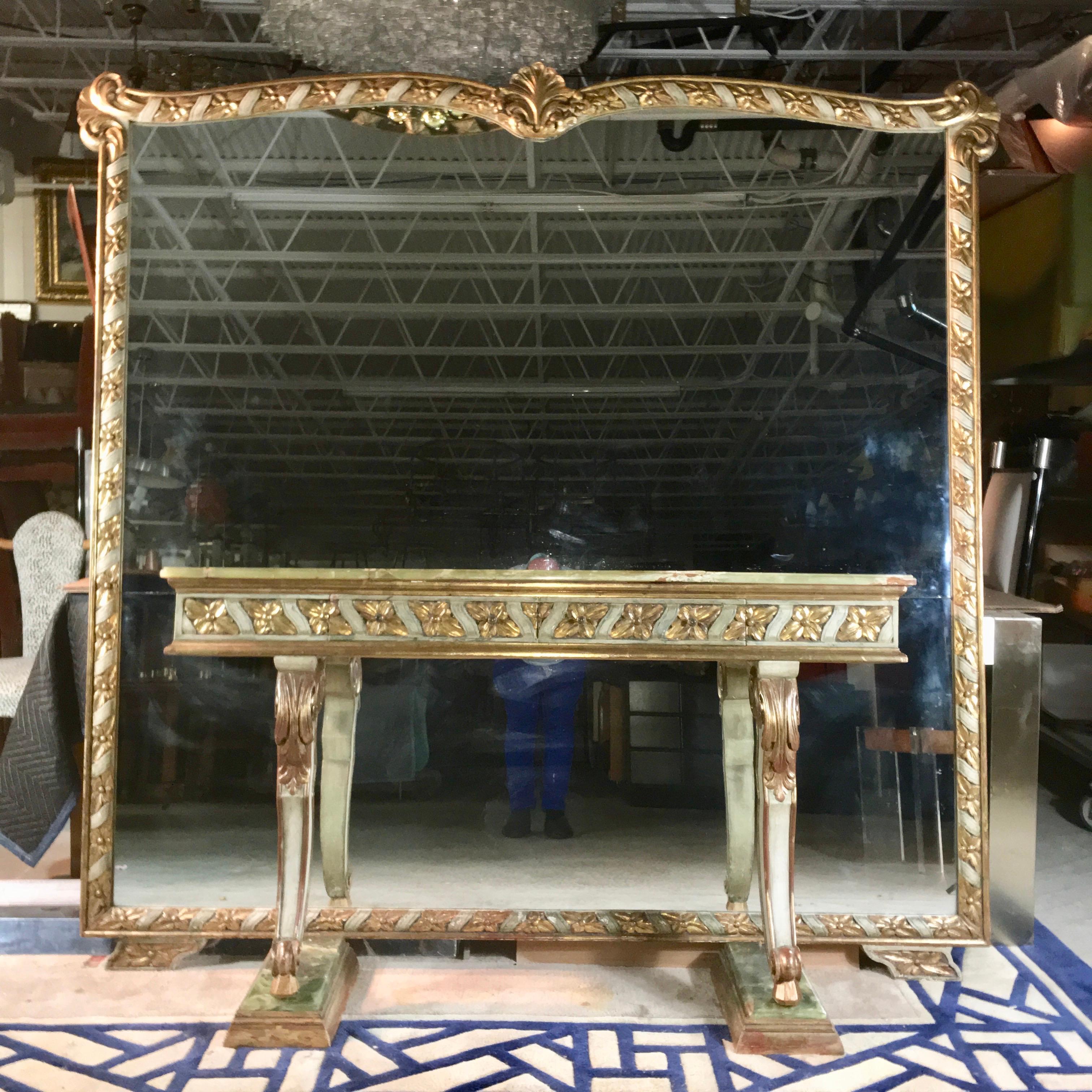 1950s vintage Italian carved, paint decorated and gilt wood framed mirror including a fixed green onyx top console table on two scrolled legs mounted on stepped onyx and gilt wood plinths.
Mirror frame appears to float above the floor on two wing