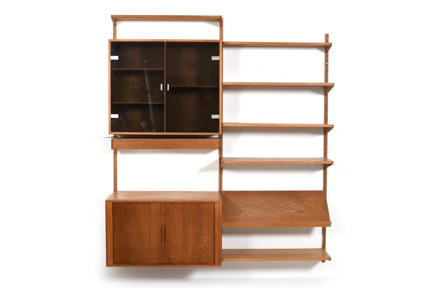 Parete attrezzata Kai Kristiansen in Oak. Include un mobile con ante in vetro e una lampada. Prodotta da Feldballes Møbelfabrik iDenmark negli anni '60. 
Il mobile a parete è composto da:
- 6 ripiani
- 1 scaffale per riviste
- 1 armadietto con porta