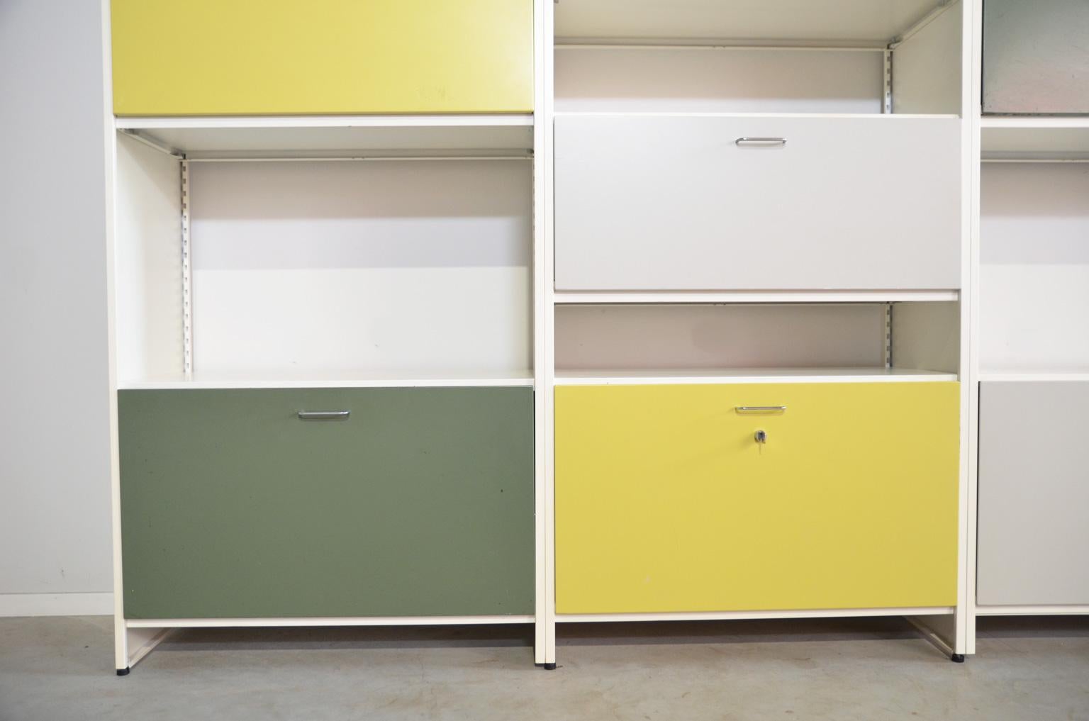 Modulair, metal wall system in the colors off-white, green, lemon and grey, with six closed storage cabinets, two small drawers and lots of shelving. This Industrial shelving unit can be used as a cabinet against the wall but also free standing as a