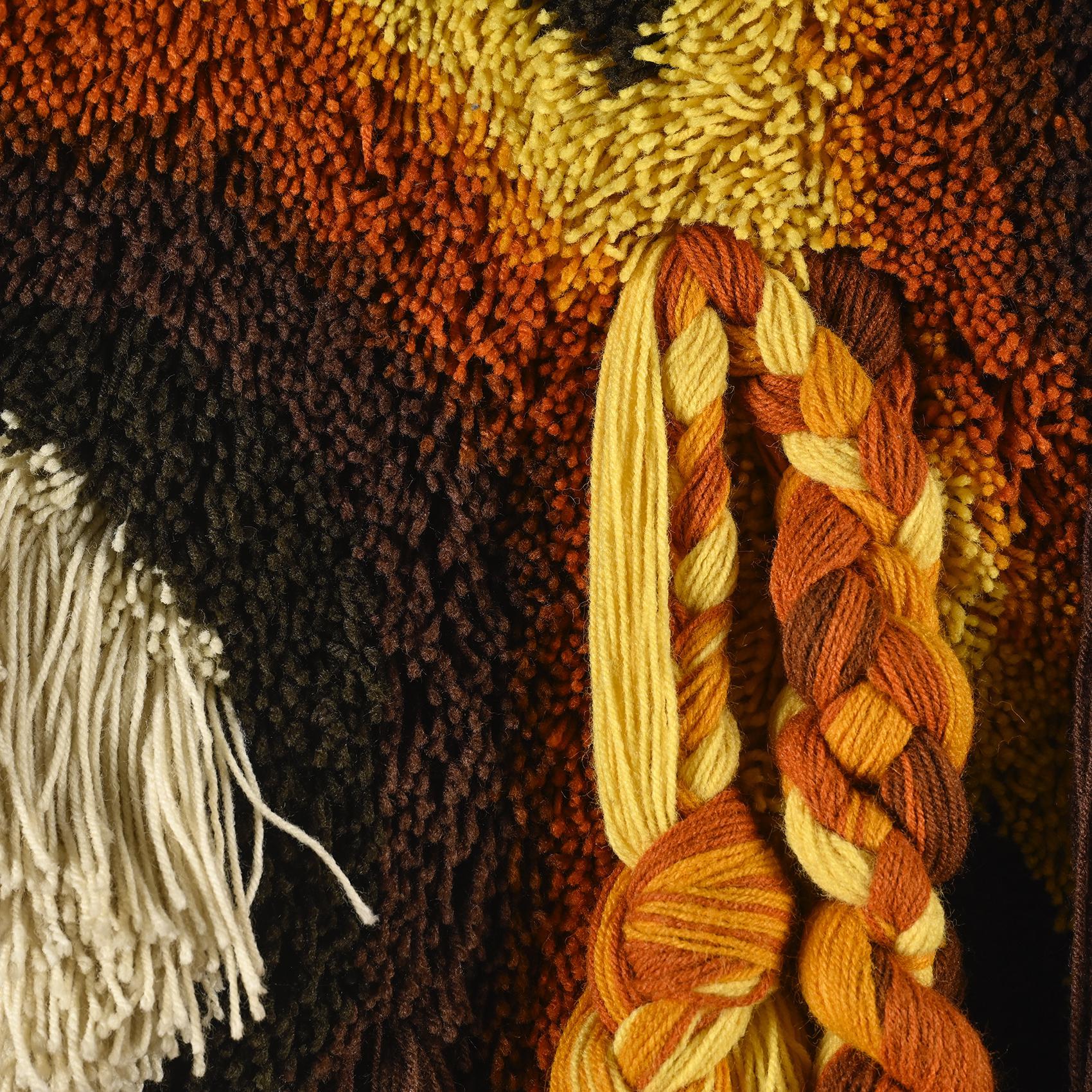 Wall tapestry in macramé, created in the 1970s and produced by Desso Studio.

Made from 100% acrylic, this wall tapestry stands out for its textured weaving, showcasing a warm palette ranging from deep brown to vibrant orange, accented with beige