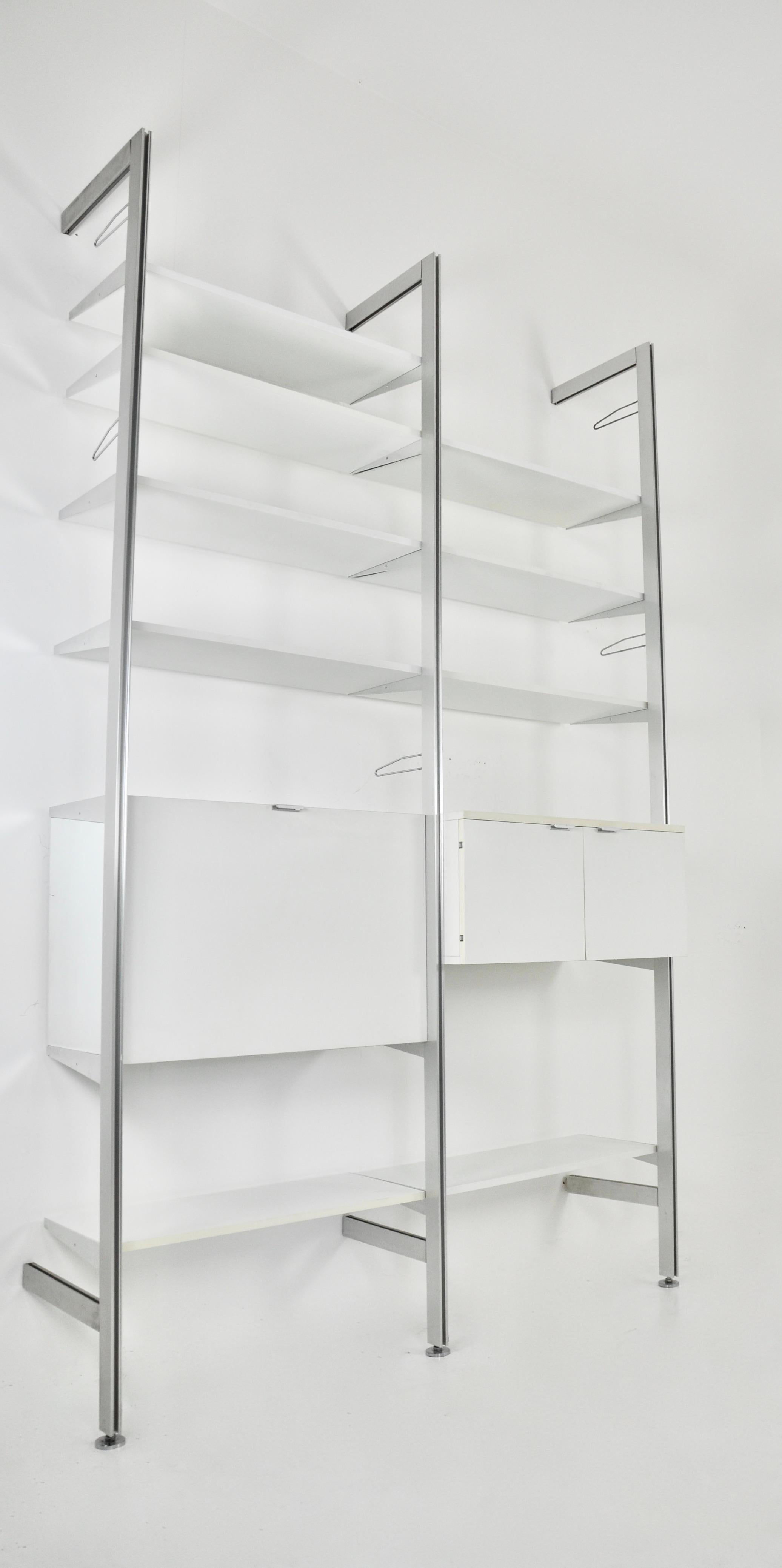 Wood and metal wall unit by Georges Nelson. It comprises 3 uprights, 9 shelves, 1 box with a folding door containing 2 drawers and storage units and 1 box with 2 doors containing a shelf. It is stamped Mobilier International. Wear due to time and