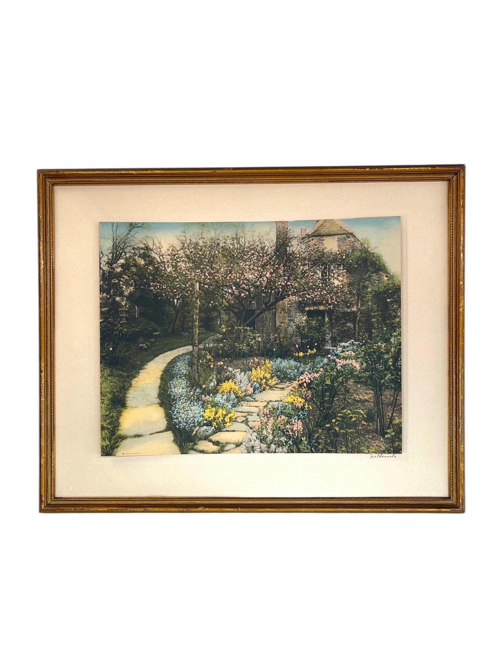  This hand-colored photograph or possibly lithograph by Wallace Nutting (1861-1941) depicts a charming garden walkway leading to a stone cottage, surrounded by blossoming trees and vibrant spring flowers. The piece is titled Nethercote, visible in