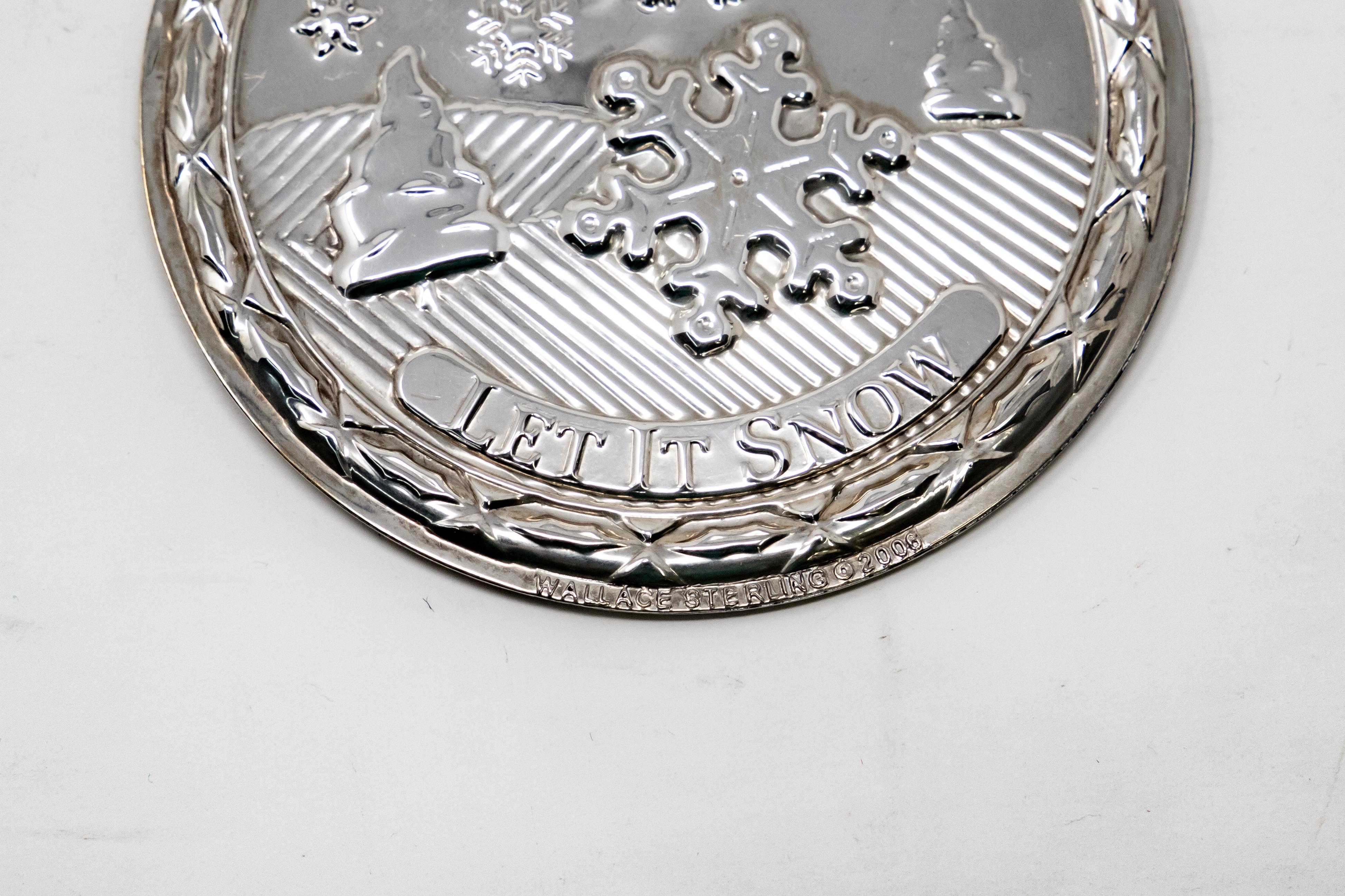 Offering a Wallace sterling silver ornament. The front depicts a landscape scene with snow falling and let it snow inscribed. The back is the same landscape with songs of Christmas inscribed. Signed Wallace Sterling with trademarks on the rim.