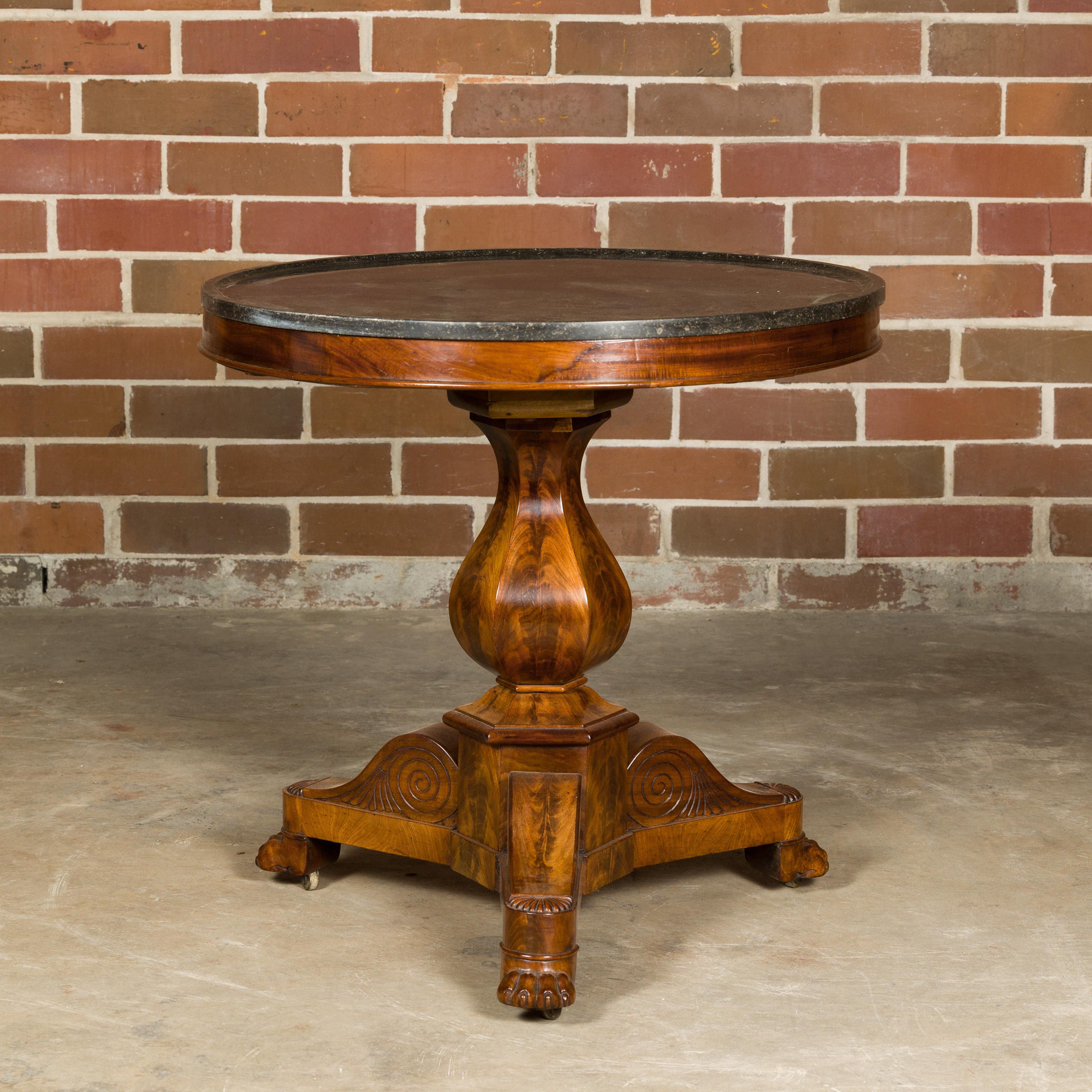 A French walnut pedestal table from the 19th century with circular black marble top, scrolling tripod base and lion paw feet. Step into the opulence of 19th-century France with this stunning walnut pedestal table. The table exudes an air of majesty,