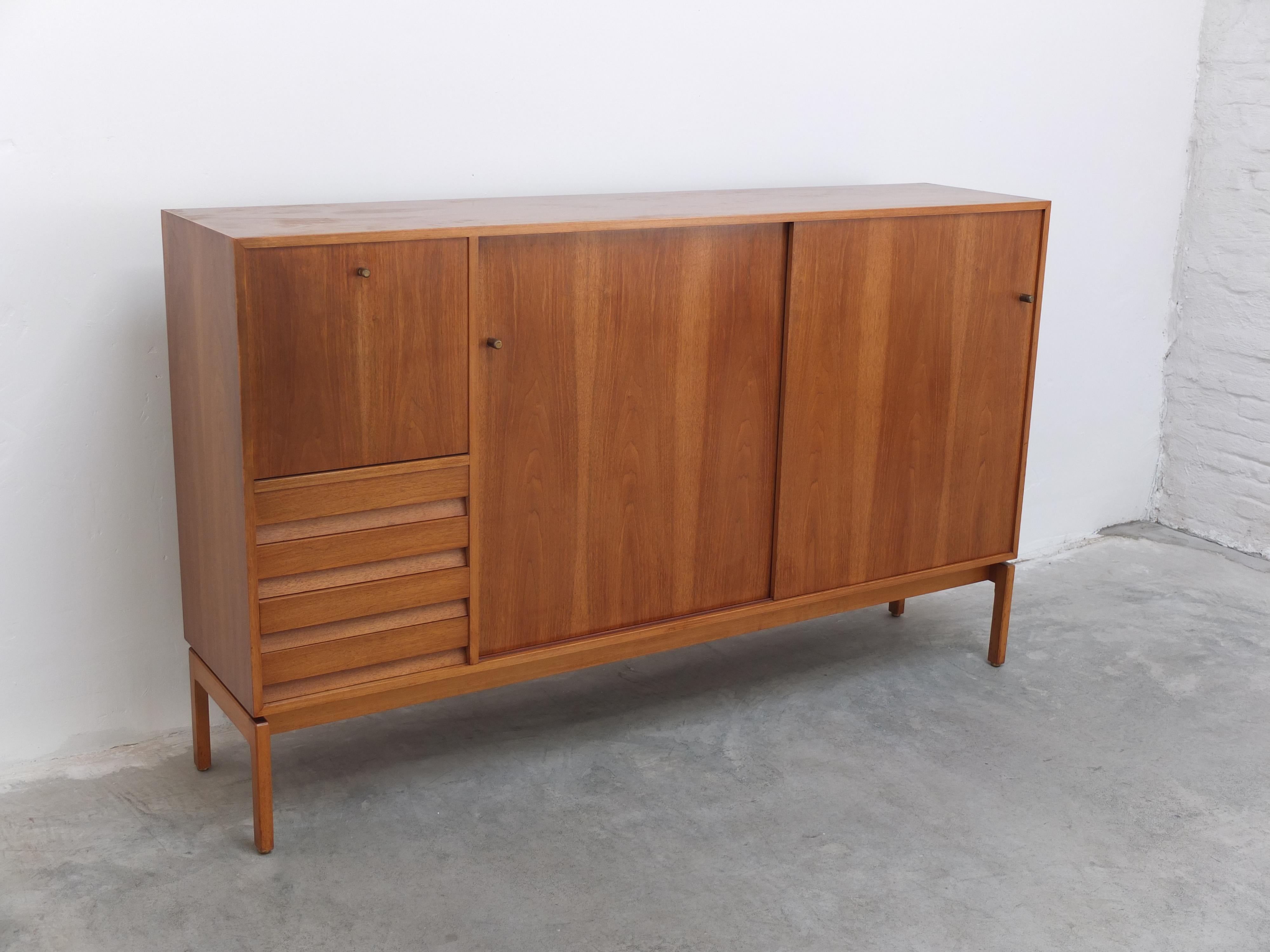 Walnut cabinet with practical sliding doors from the ‘Abstracta’ series designed by Jos De Mey for Van Den Berghe-Pauvers during the 1960s. The beautiful wood grain combined with the signature drawers and brass pulls make this a highly decorative