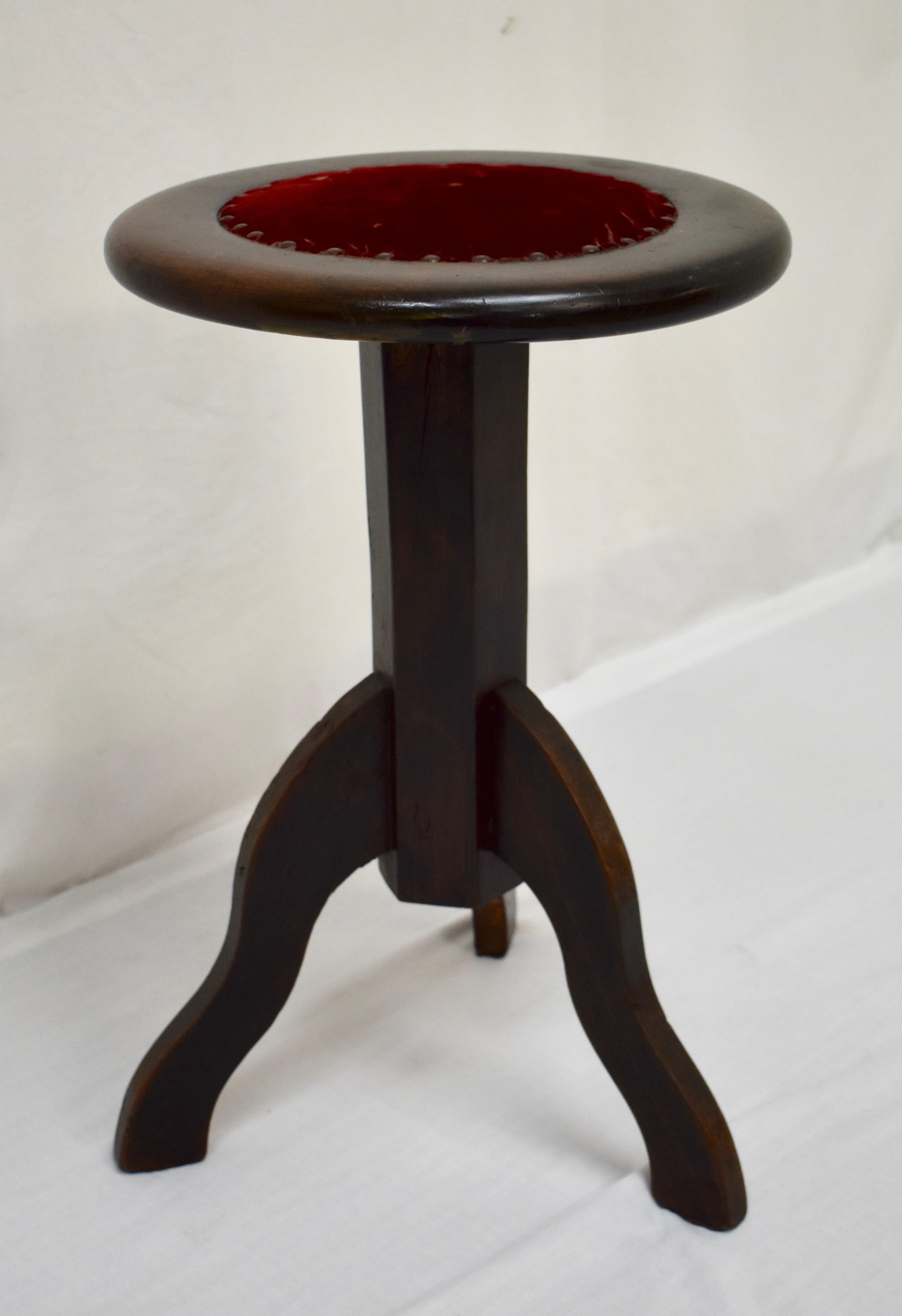 This sturdy tripod walnut stool has a generous seat with a worn red velvet insert. The base is a plain hexagonal column mounted on three wavy legs, the column concealing the iron screw thread which allows the seat to adjust to close to 30” (bar