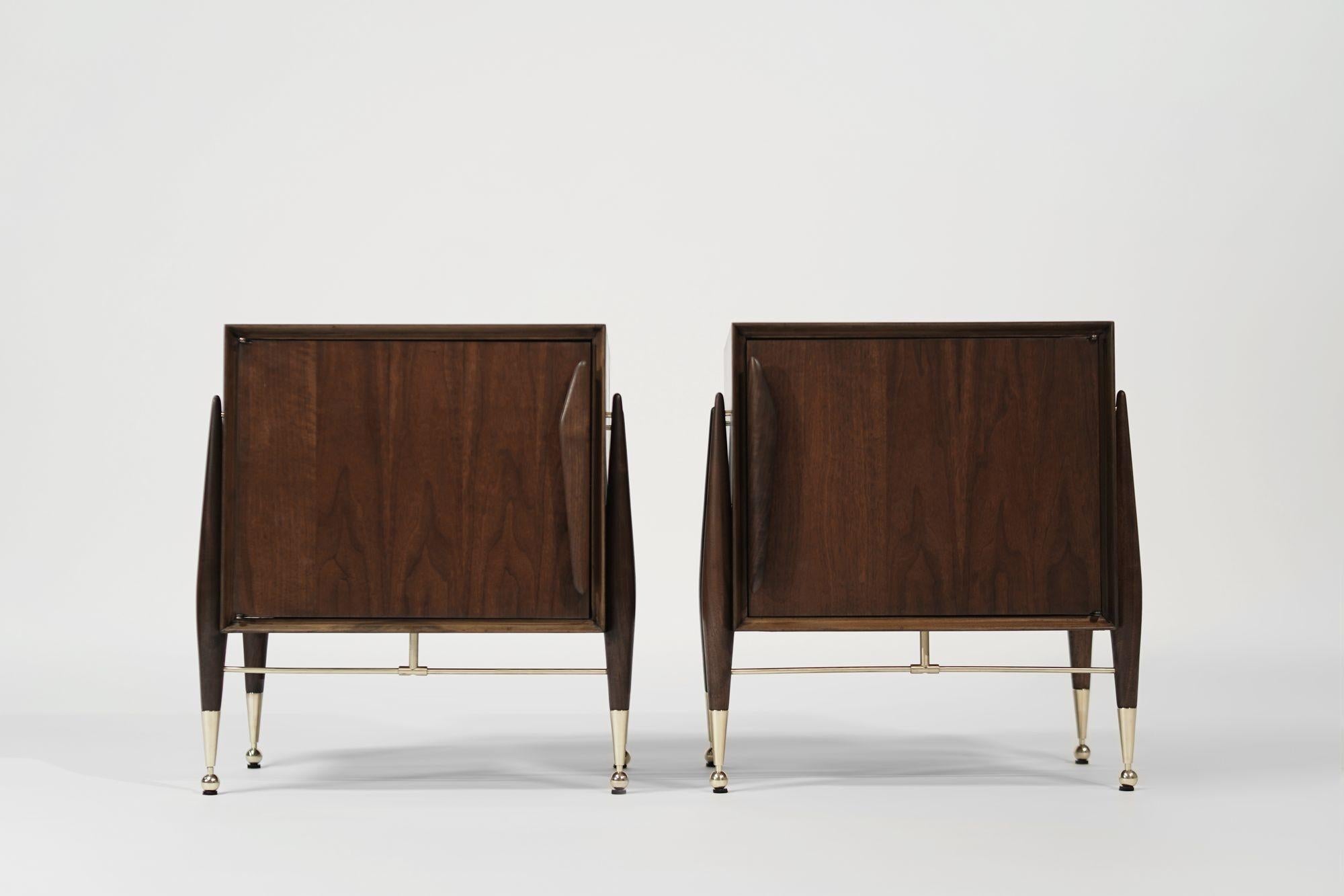 Un superbe ensemble de tables d'appoint en noyer et laiton par Kent Coffey, vers les années 1950, méticuleusement restauré par Stamford Modern. Dotée de poignées de tiroirs sculptées, chaque porte s'ouvre pour révéler d'élégantes étagères en verre,