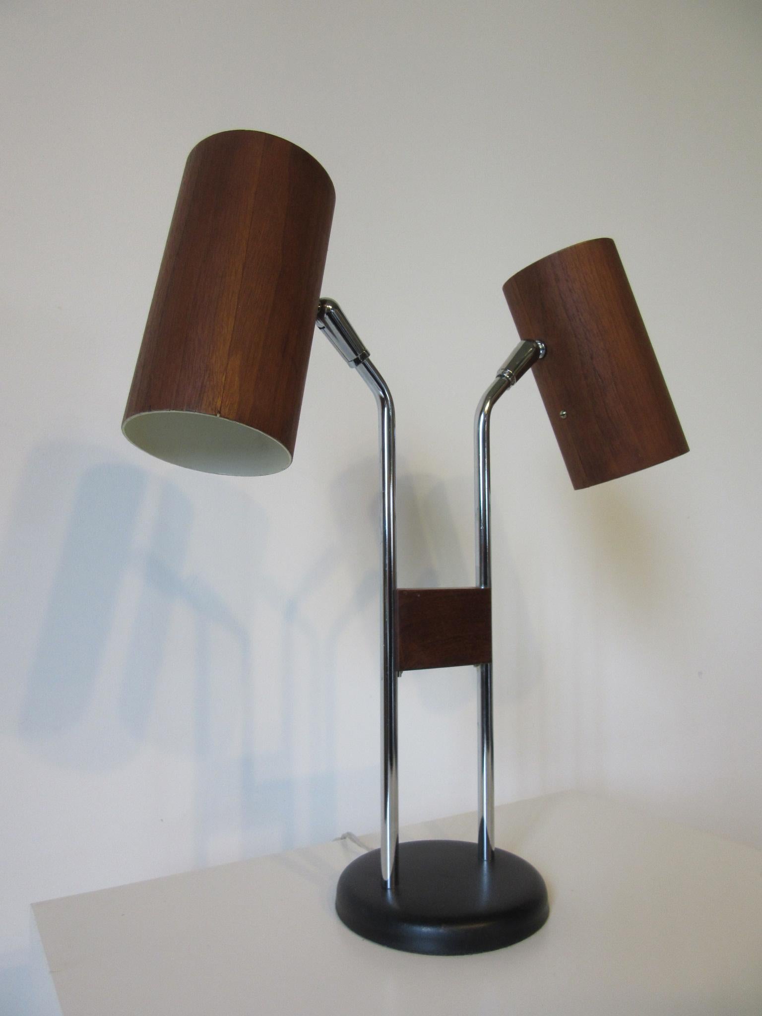 An adjustable swiveling double-headed table lamp with walnut veneer wrapped cylinder shades mounted on polished chromed stems held together by a piece of walnut with a satin black metal base. The three-way light switches to the tops of each cylinder