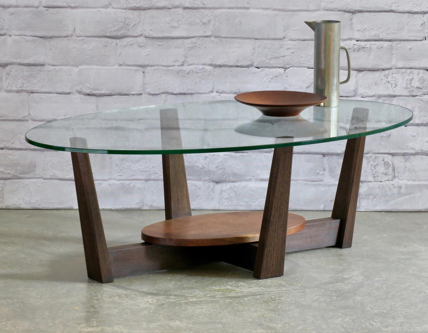 Cette nouvelle table basse ovale Afilar se caractérise par un piètement en noyer noirci sublimement rectiligne supportant un plateau en verre de 1/2