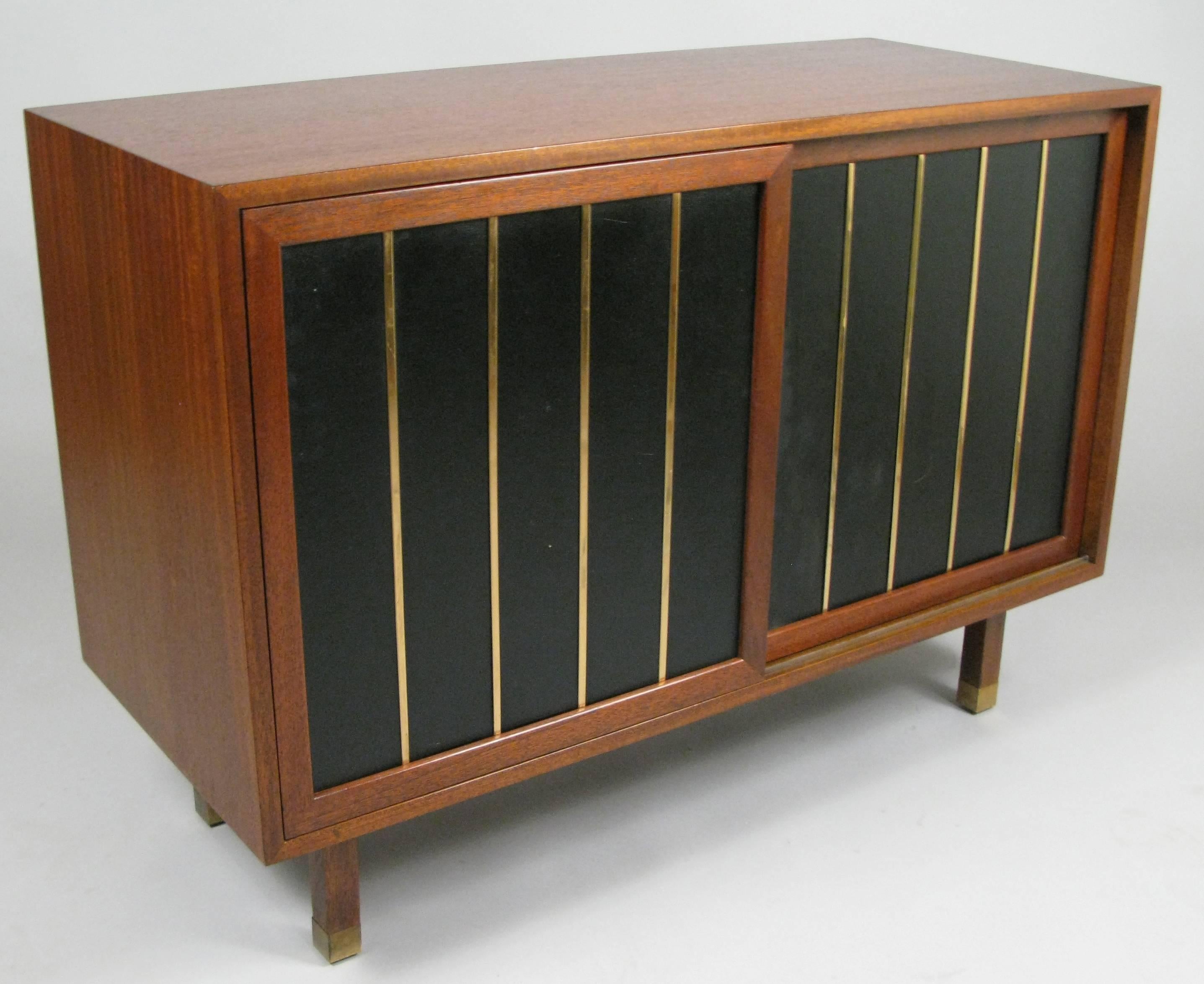 A beautiful and unique 1950s walnut cabinet by Harvey Probber. With sliding doors covered in leather and brass trim, raised on walnut legs with brass sabots. Each side of the cabinet has three drawers.