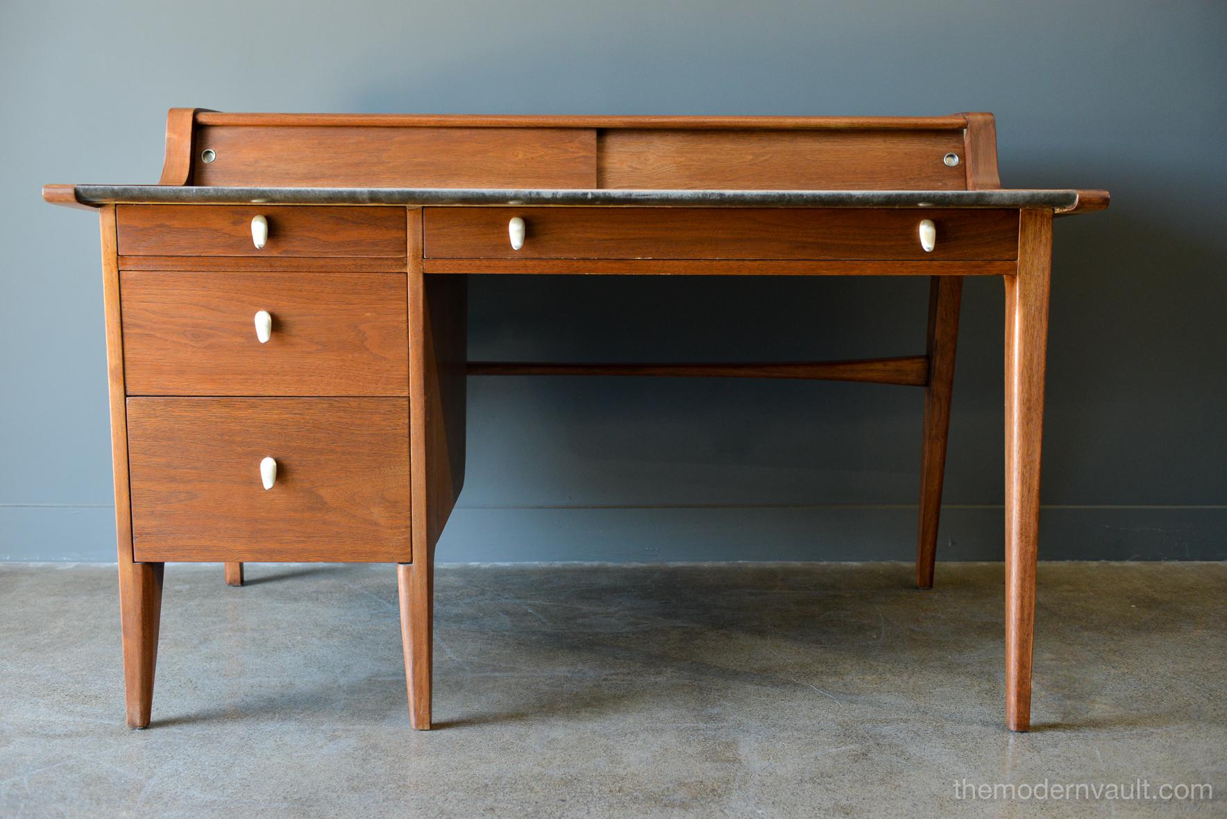 Walnut and leather top desk by John Van Koert for Drexel, circa 1960. Model K80. Very Good original condition with original grey leather writing top. Two sliding smaller doors with a lower slanted file drawer and three other drawers offer plenty of