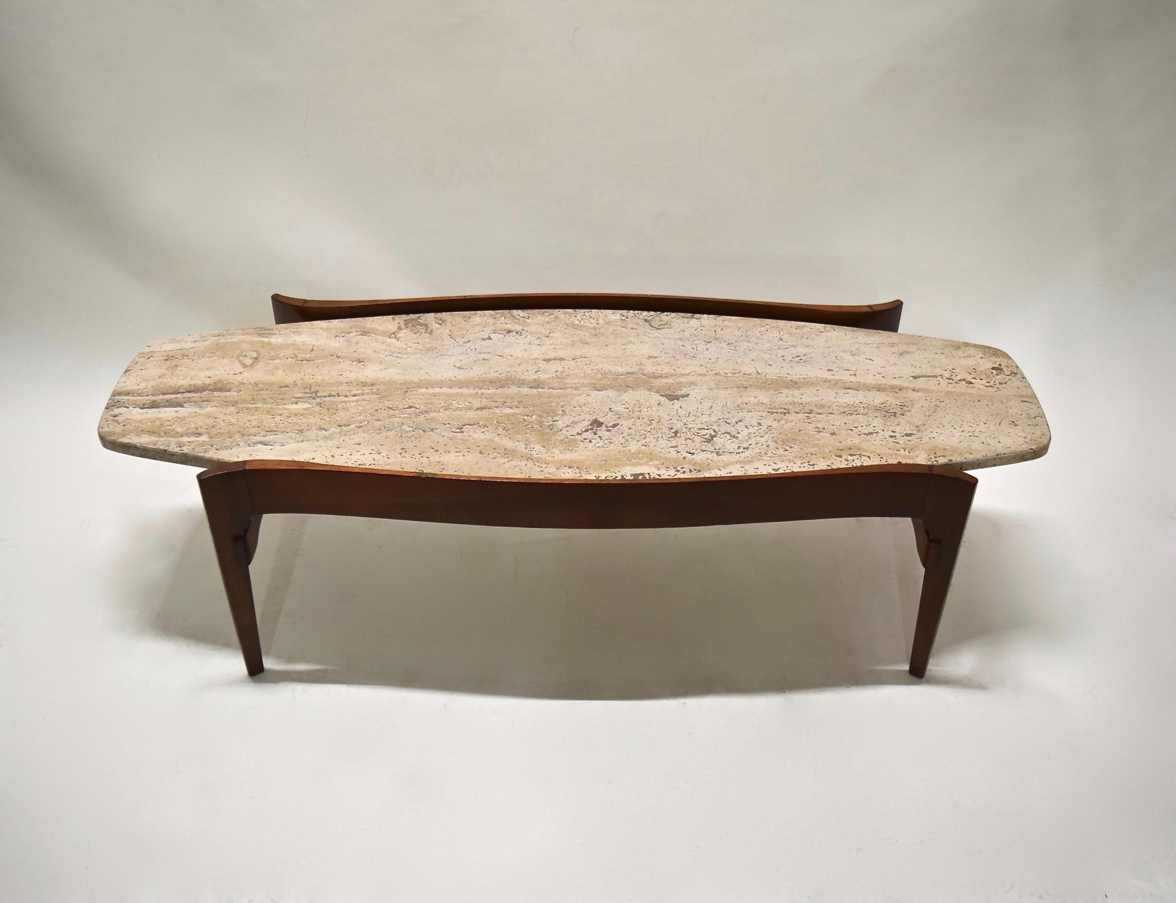 Oblong coffee table with a walnut frame that has a curving apron, four tapered legs and two supportive stretchers and an Italian travertine top. Labeled on the underside.