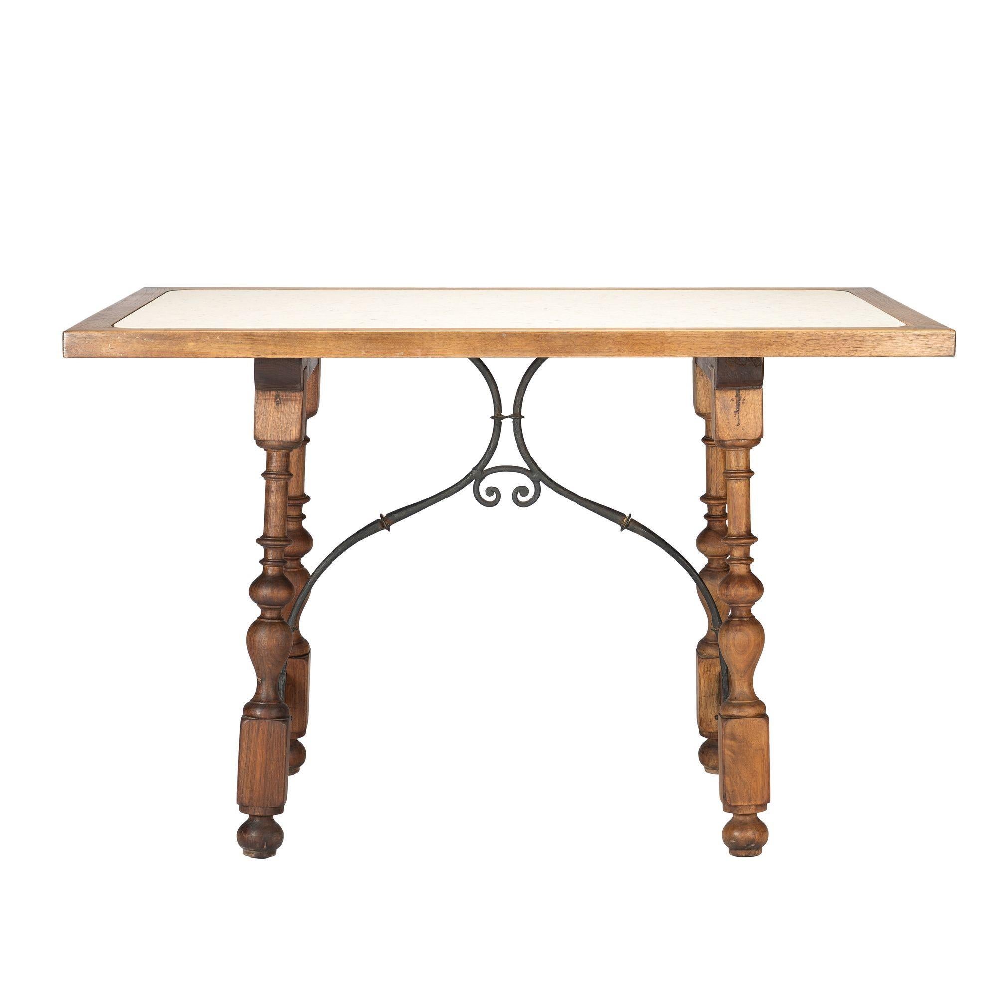 Spanish Baroque style walnut and travertine marble table. The travertine marble top is set in a walnut frame on four turned legs. The vigorously turned walnut legs are joined by turned stretchers and braced with a hand forged arched iron bracket in