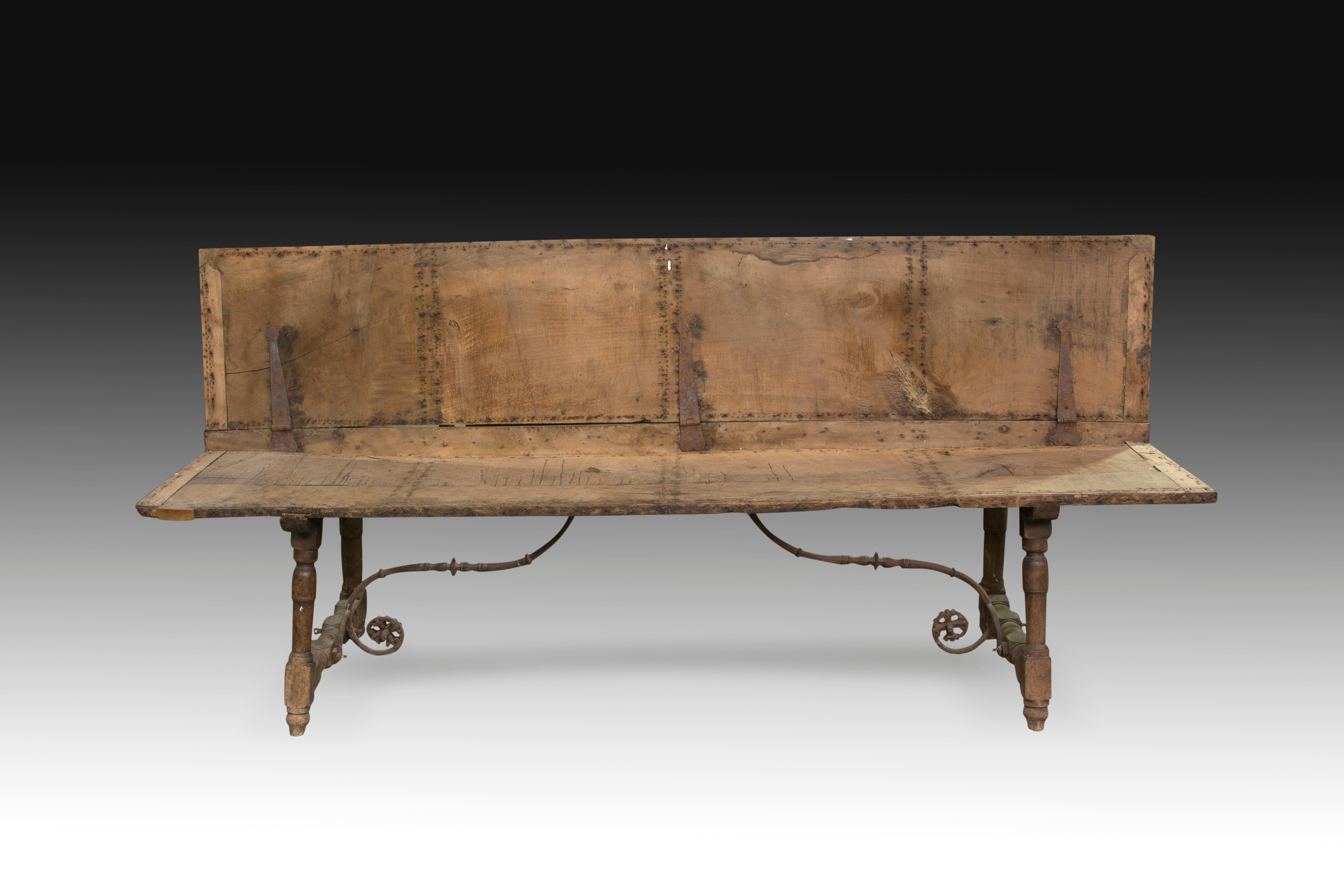 Wrought iron fork-shaped fasteners.
Requires restoration.
Bench (with folding backrest in origin) made of carved walnut wood and reinforced with wrought iron fittings on the back and legs (these two curved, decorated with disks and 