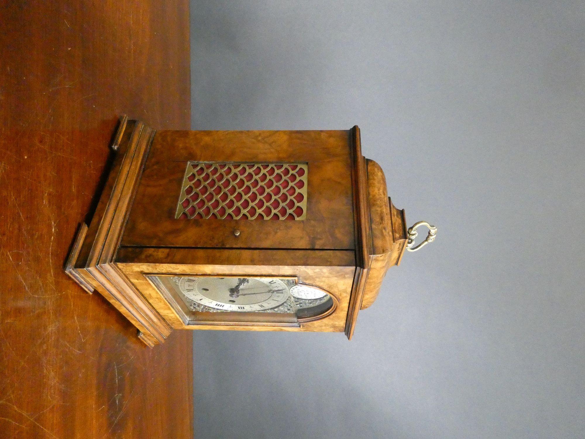 Walnut Westminster Chiming Mantel Clock
Finely figured bell top walnut case standing on a stepped moulded plinth with block feet. Brass silk lined sound frets to the sides and rear door, surmounted by a decorative carrying handle.
Hinged front door
