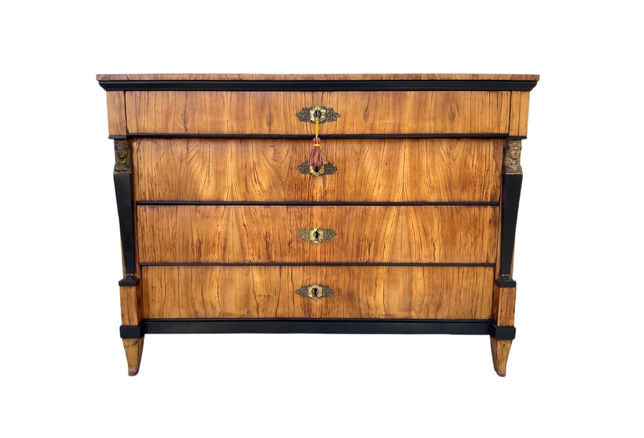Biedermeier walnut chest of drawers/commode. This stunning piece has four large drawers. Drawers have brass hardware and are flanked by black ebonized columns with classical headed figurines. Chest is raised on four short flaring feet. Wonderful