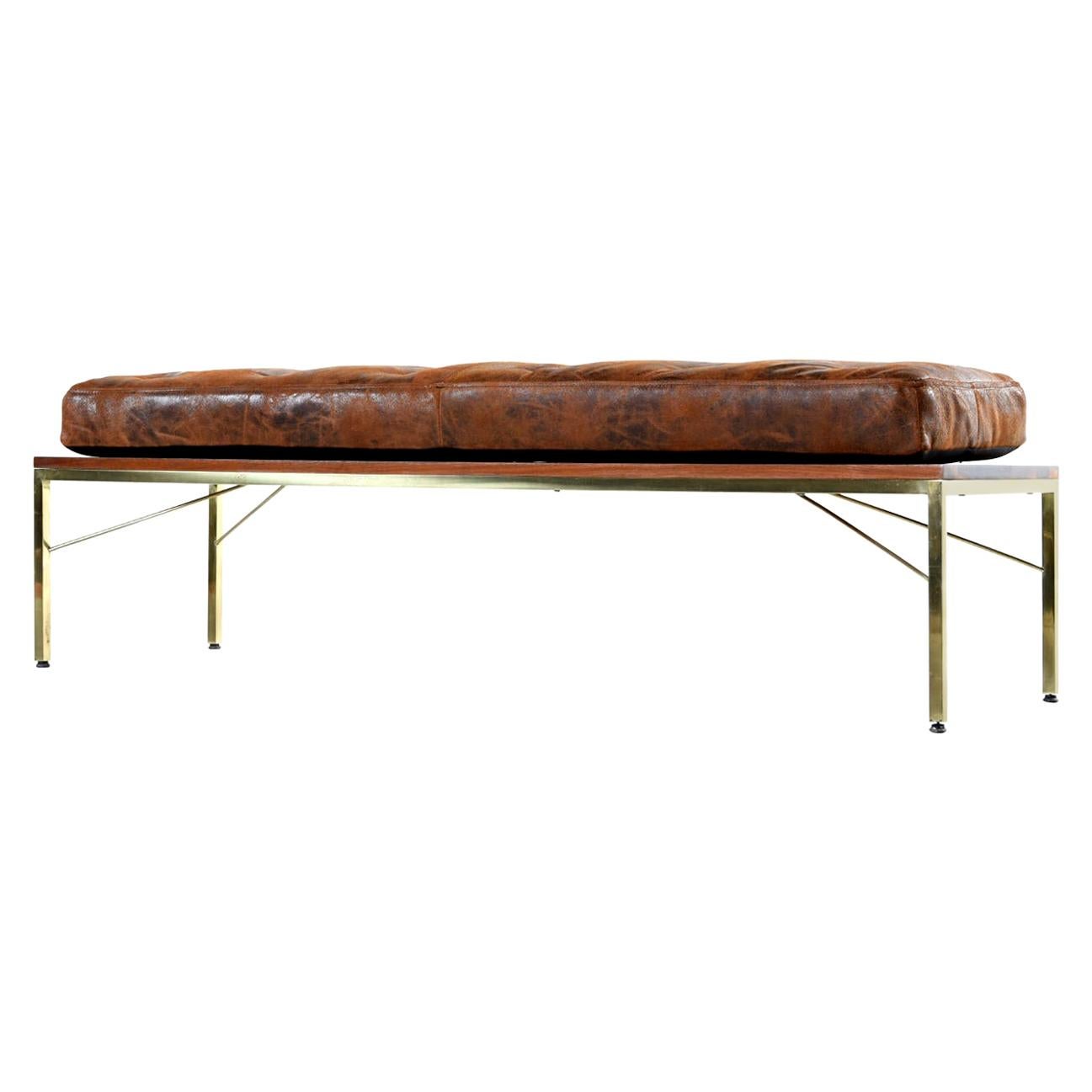 This Mid-Century Modern coffee table doubles as a bench with the addition of a newly fashioned leather cushion. The vintage 1950s era coffee table is reminiscent of Paul McCobb’s gold base ottomans. This piece features a stylish gold base with