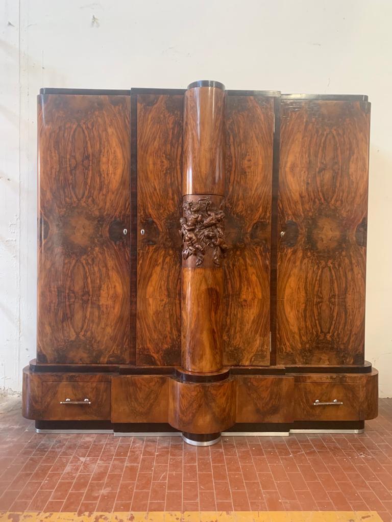 Art deco closet in walnut. 3 Doors, door in the center door mirror inside. Wavy lines, the base is surrounded by steel profile. The center stands high relief of allegory of festive putti, masterfully carved. Opening with key brings signs of holes of