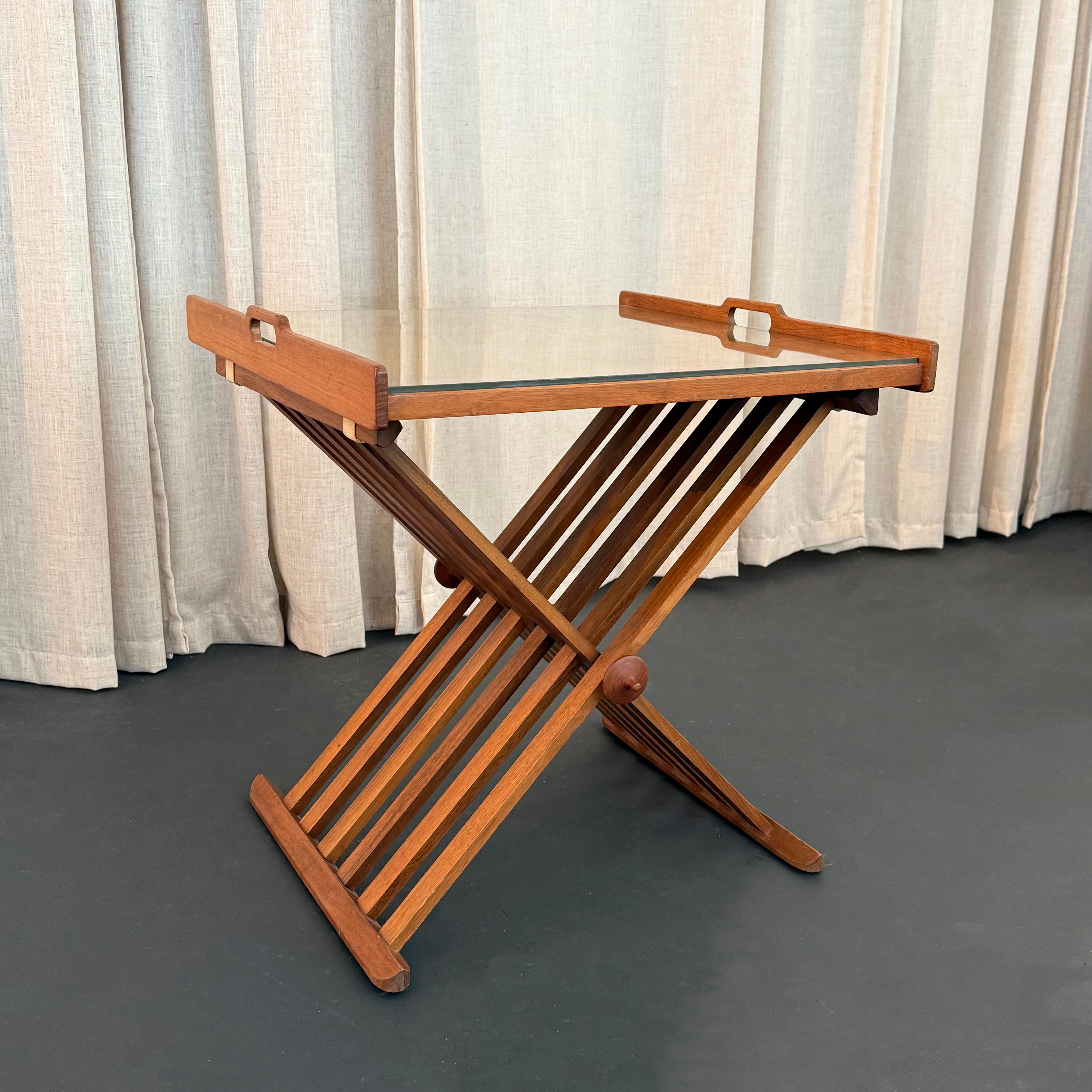 This Mid-Century Modern folding walnut and glass campaign tray table was created by two designers Stewart MacDougall and Kipp Stewart for the Drexel Furniture Company during the late 1950s. MacDougall and Stewart designed this model number 881-401