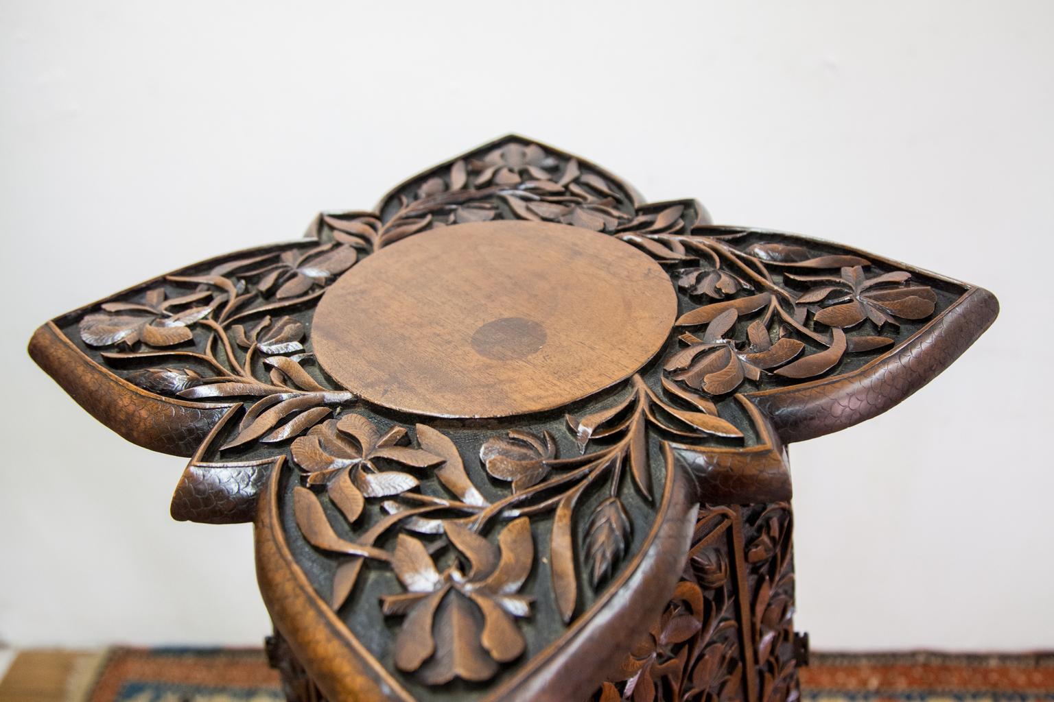 Walnut carved plant stand has floral leaf and vine designs on all sides carved in high relief. There is carved fish scale molding on the top.