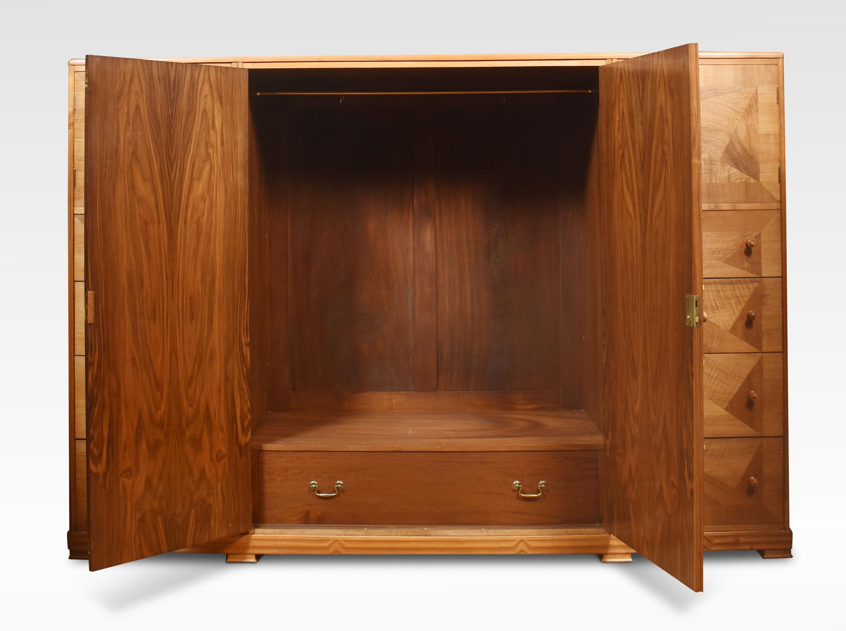 Walnut combination wardrobe, the moulded top above two long panelled well-figured doors opening to reveal the large hanging area flanked by two banks of drawers with stylised walnut handles and cupboards above. All raised up on a plinth base.