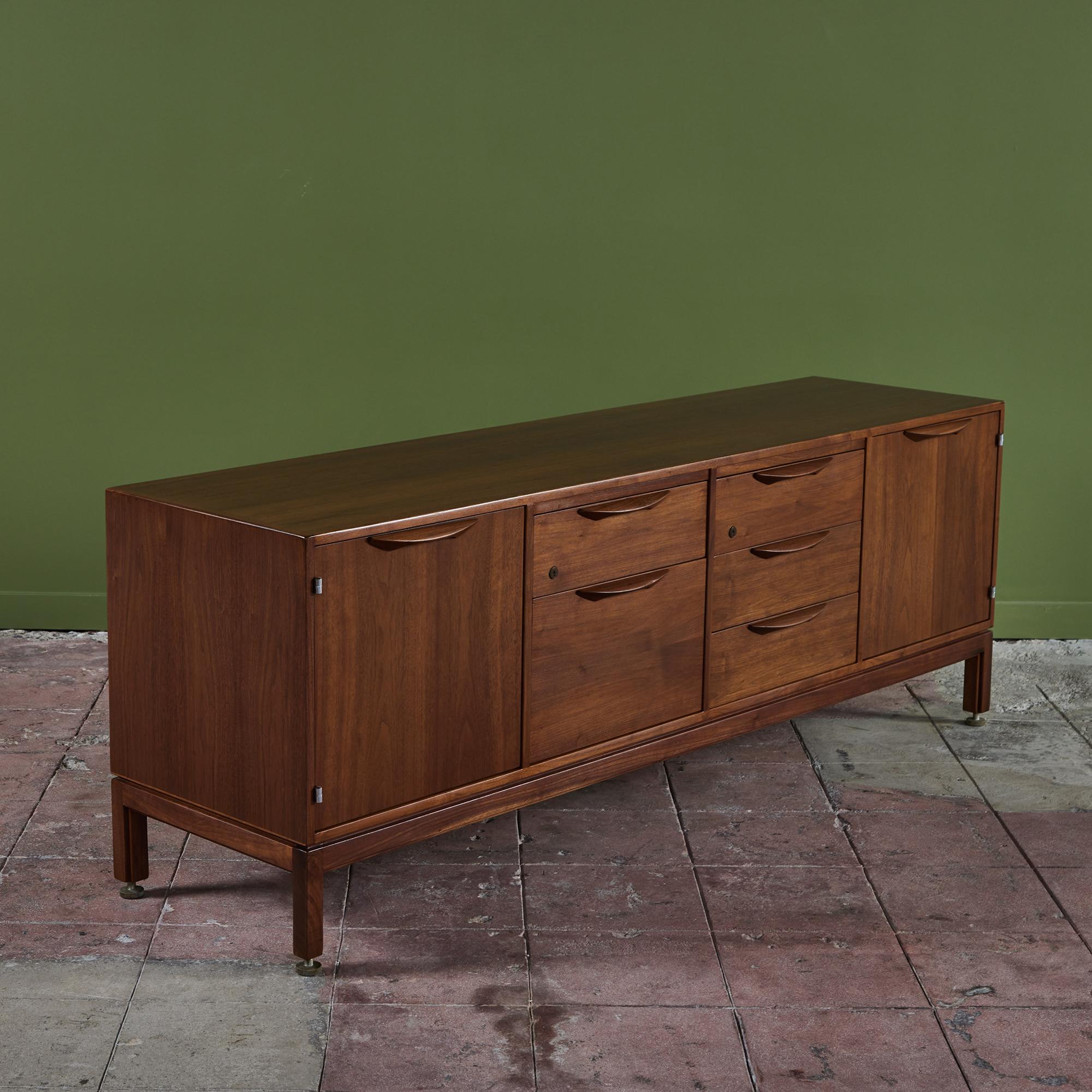 Designed by Jens Risom, USA, c.1960s. This Walnut credenza features two compartments with door fonts and interior adjustable shelves. At the center of the credenza are five drawers, one of which is rather deep and two that are divided into