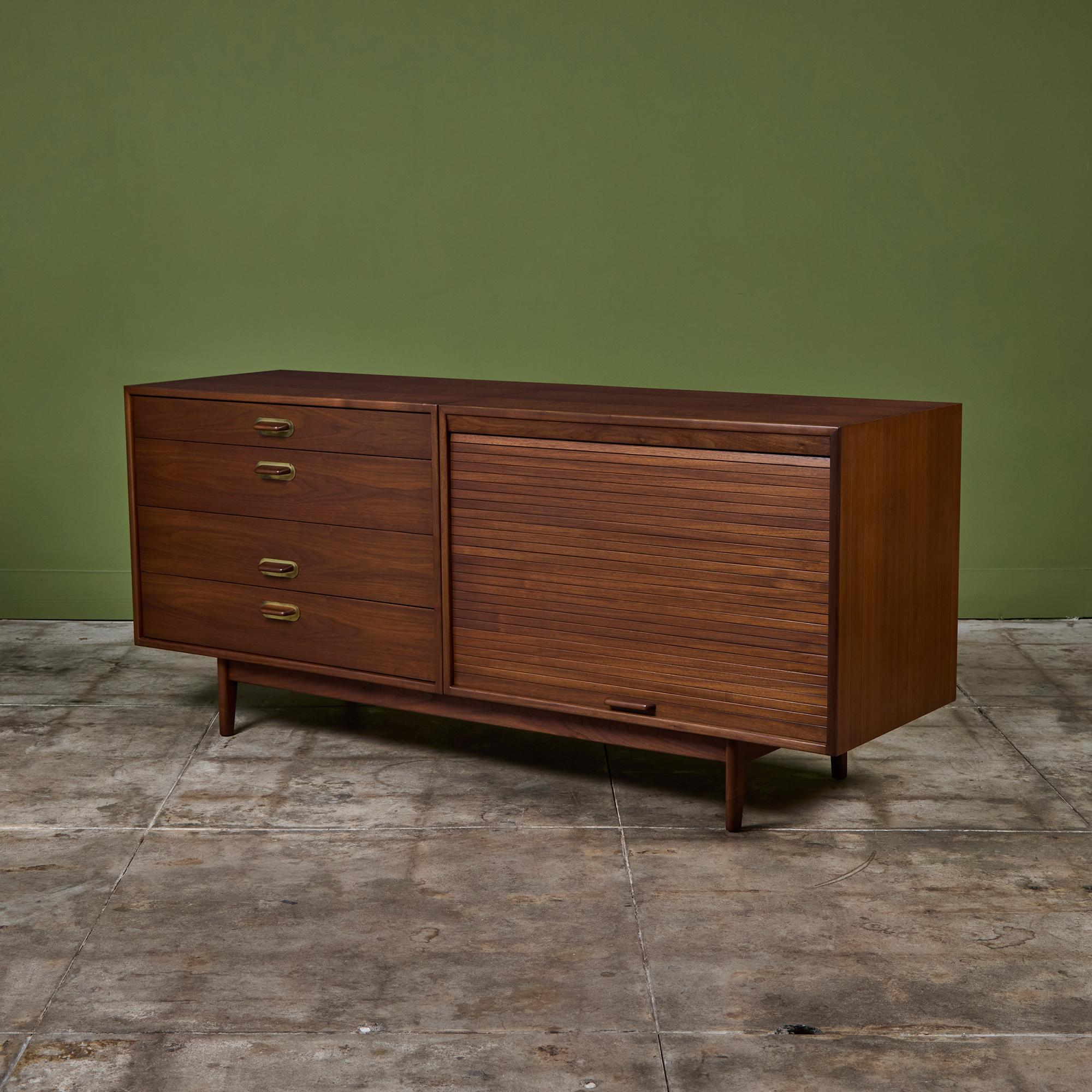 Designed by Jens Risom, c.1960s, USA. This four drawer walnut credenza features one side of drawers and two shelves concealed by a roll top tambour door. The walnut handles have a brass plate detail. The unit rests on four tapered