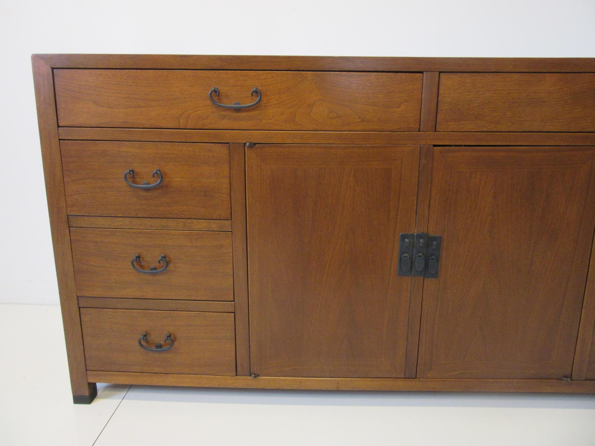 A rich medium colored walnut credenza / cabinet with six smaller drawers to each side , two larger top drawers and two middle doors with a shelve and storage . All having satin black metal pulls and retains the original hanging paper tag from the