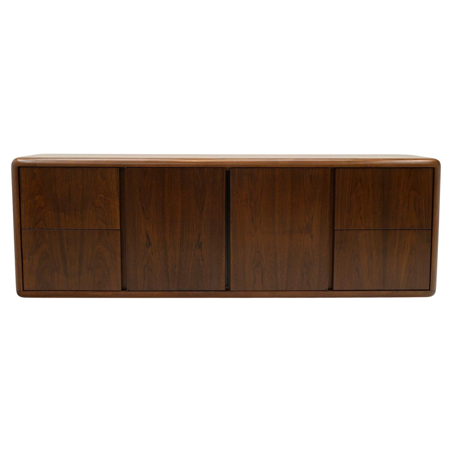 Four door walnut credenza floating on a chromed recessed base manufactured by Office Suites, Inc, 1960s.  Beautiful restored and refinished condition.    The two center doors reveal a wide adjustable shelf and the two outer doors reveal a pair of