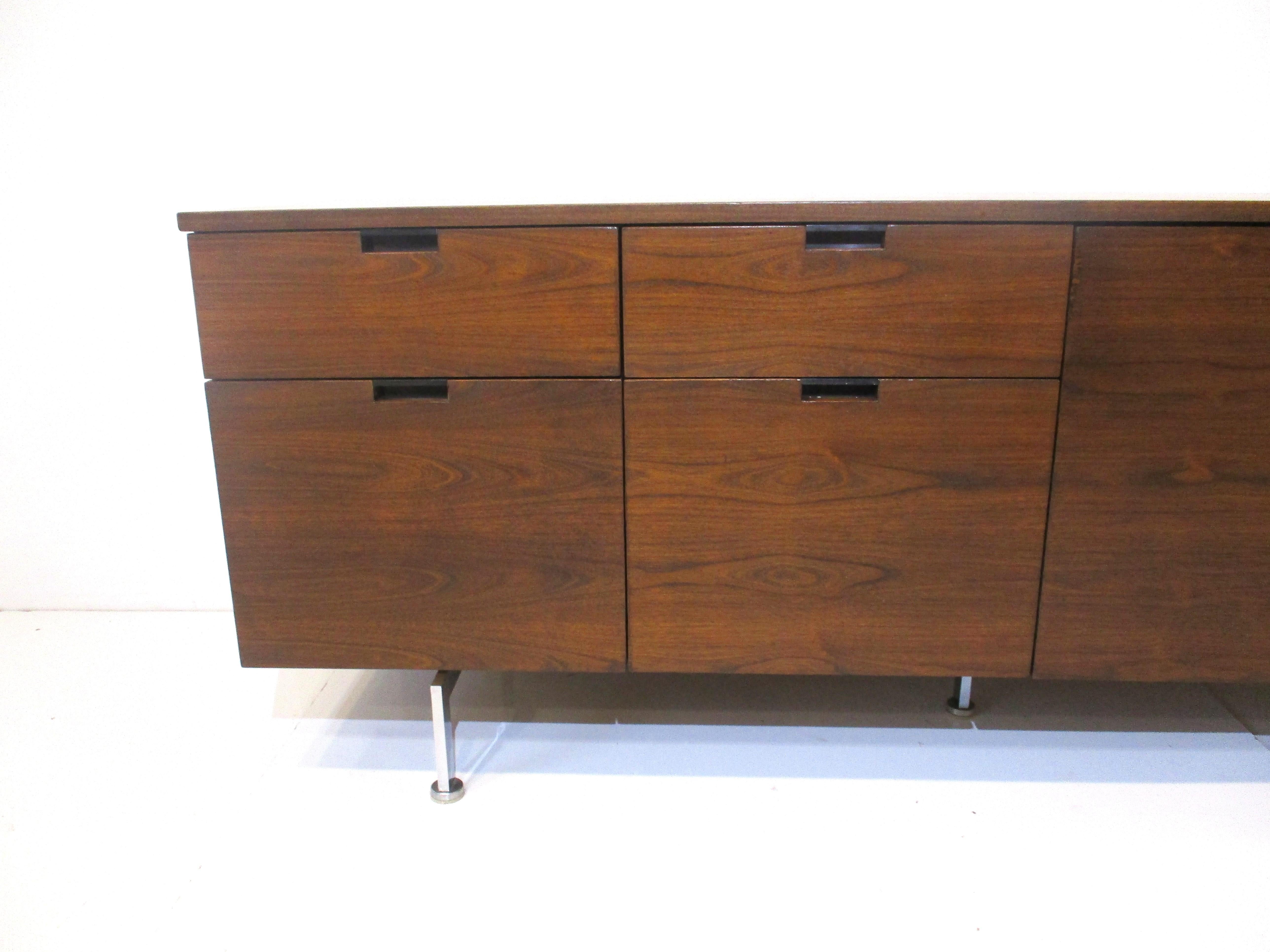 A Mid Century credenza in a medium dark walnut with two small drawers , two larger drawers and double push open and slide doors having one adjustable shelve . The pulls are in a satin black metal with cut out for your fingers all sitting on cast