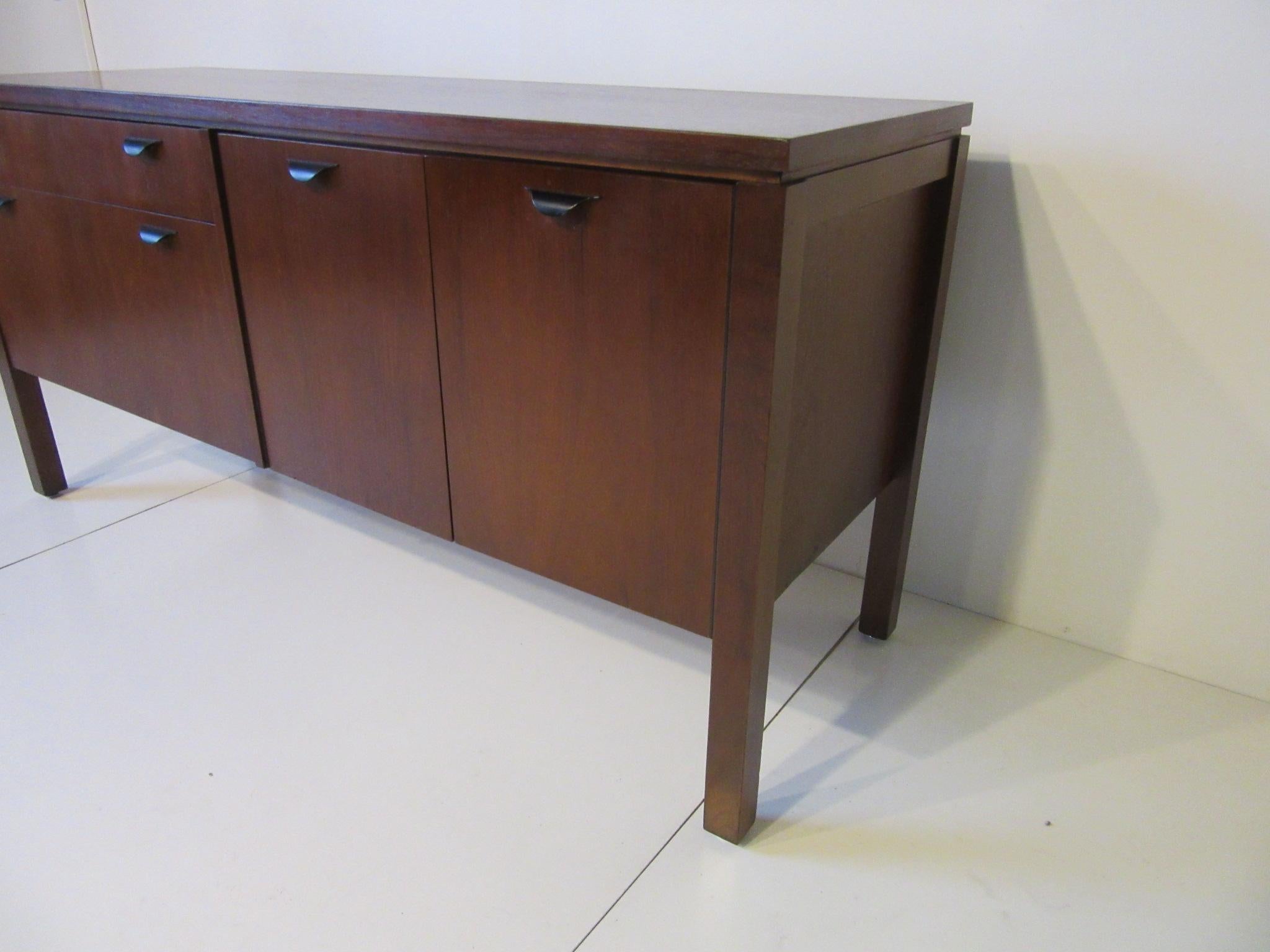 A dark walnut credenza or server with double doors, adjustable shelve and two drawers all having curved satin black pulls. The backside is finished designed in the manner of Jens Risom.