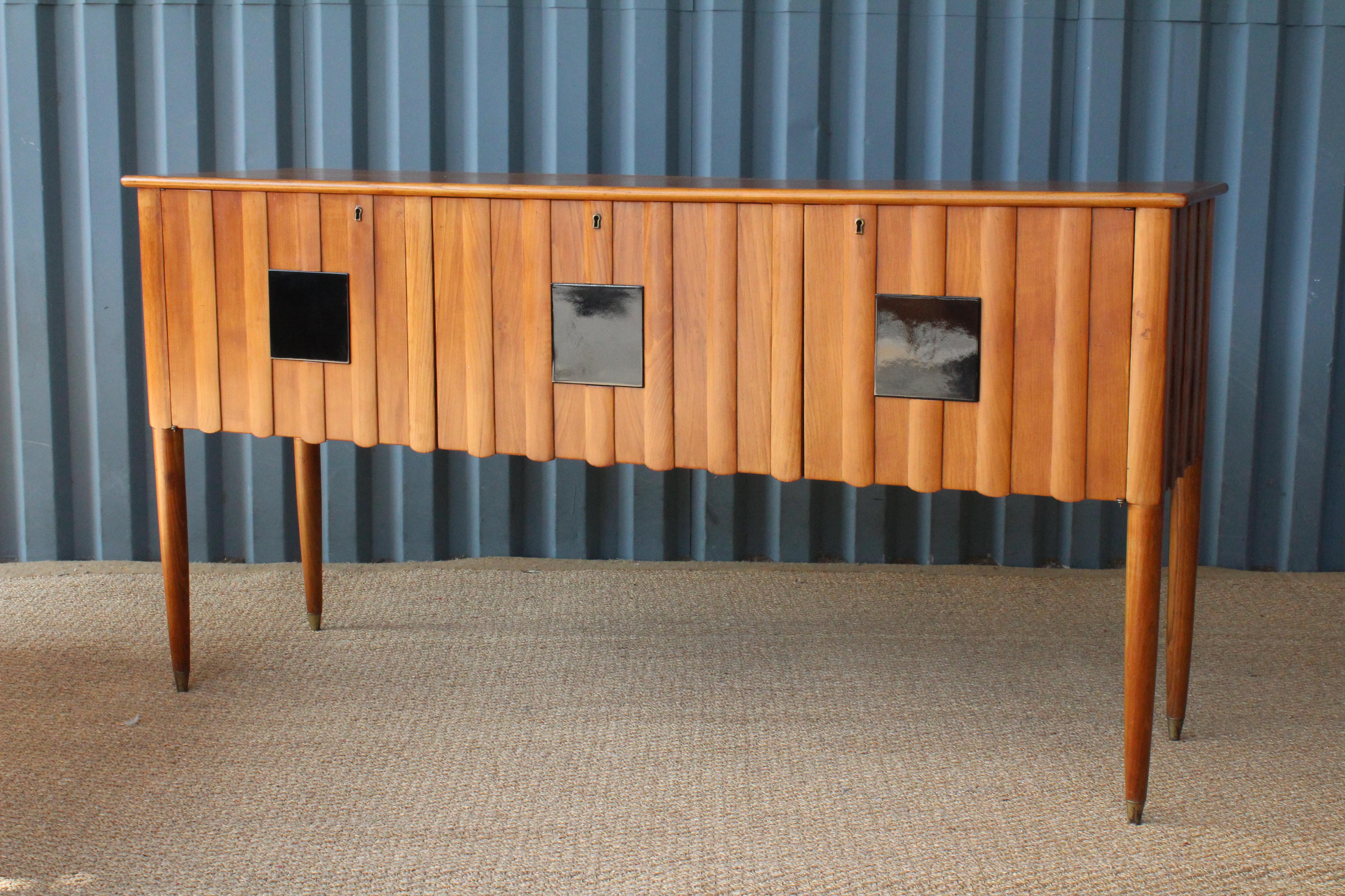 1950s Italian credenza with locking doors. This piece has a center compartment which was used to hold bar ware. This piece has the original red glass and mirrored tiles in the interior center compartment. Black lacquered wood tiles on the front of