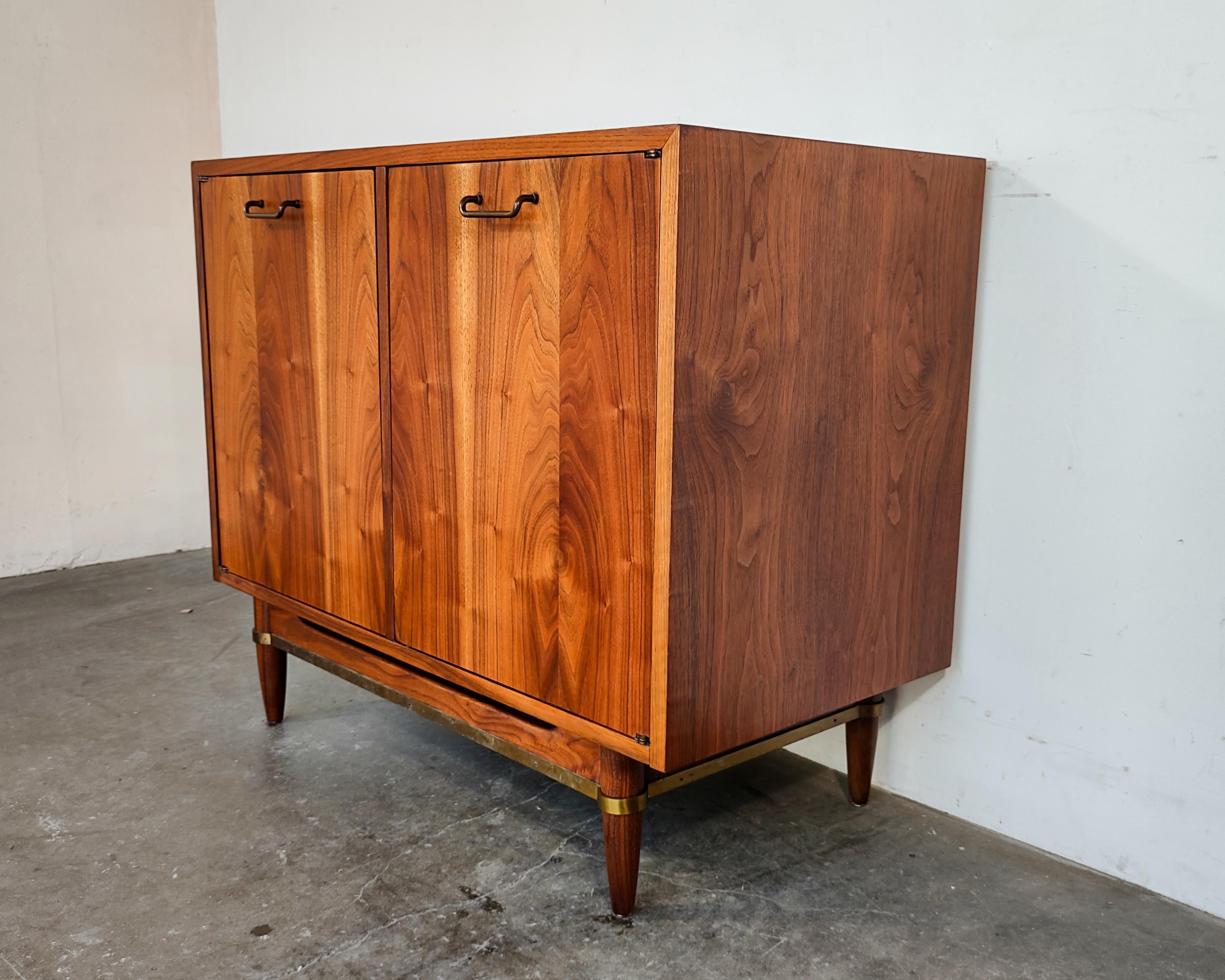 1960s American of Martinsville cabinet with brass hardware from the 'Dania' collection. Completely refinished to showcase beautiful walnut wood grain. Interior features fixed shelf on left and two classic contrasting mid-century