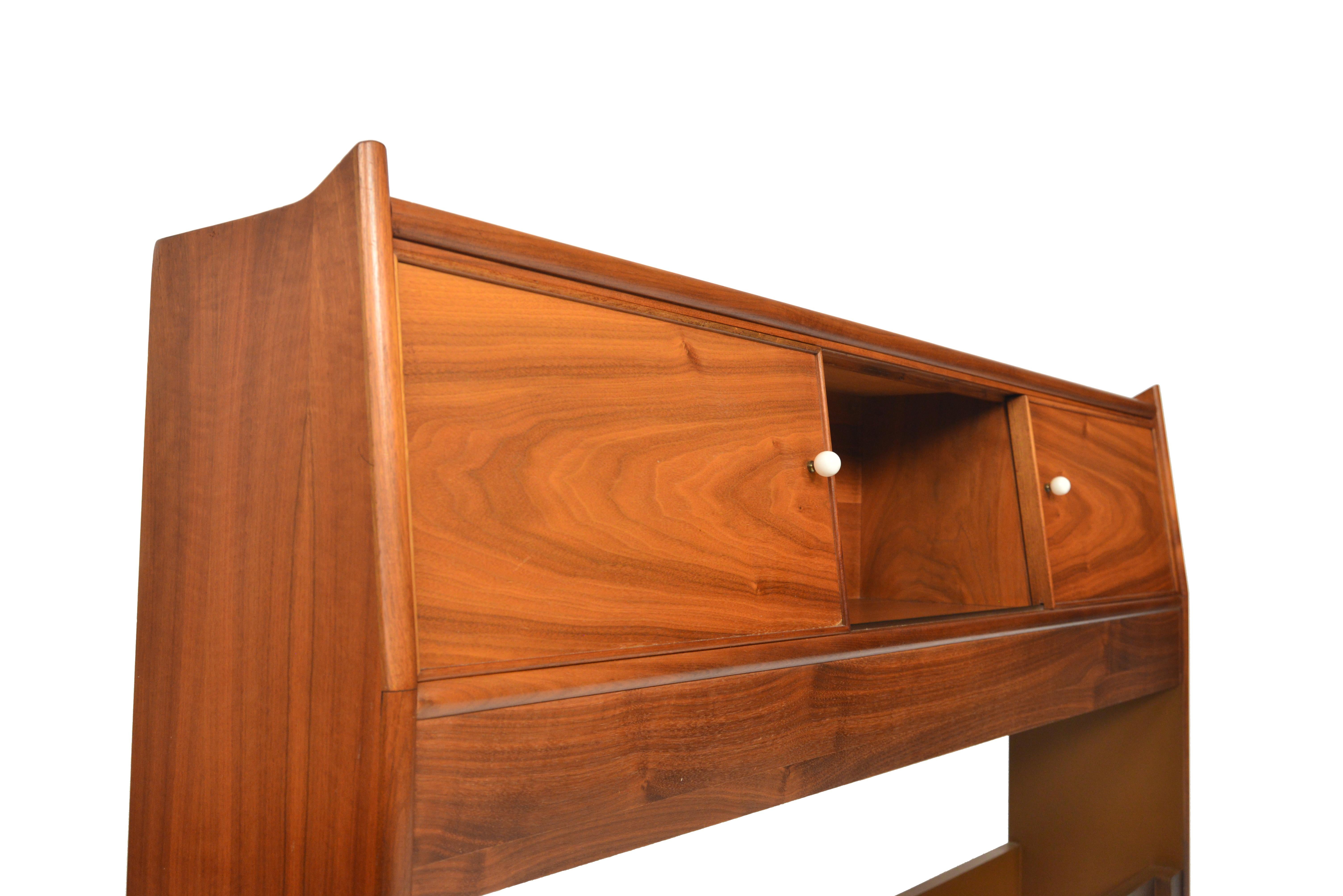 This midcentury walnut full sized headboard was designed by Kipp Stewart for the Drexel’s ‘Declaration’ range in the late 1950s. Tastefully detailed, this headboard offers three bays of storage with sliding doors adorned with the original white