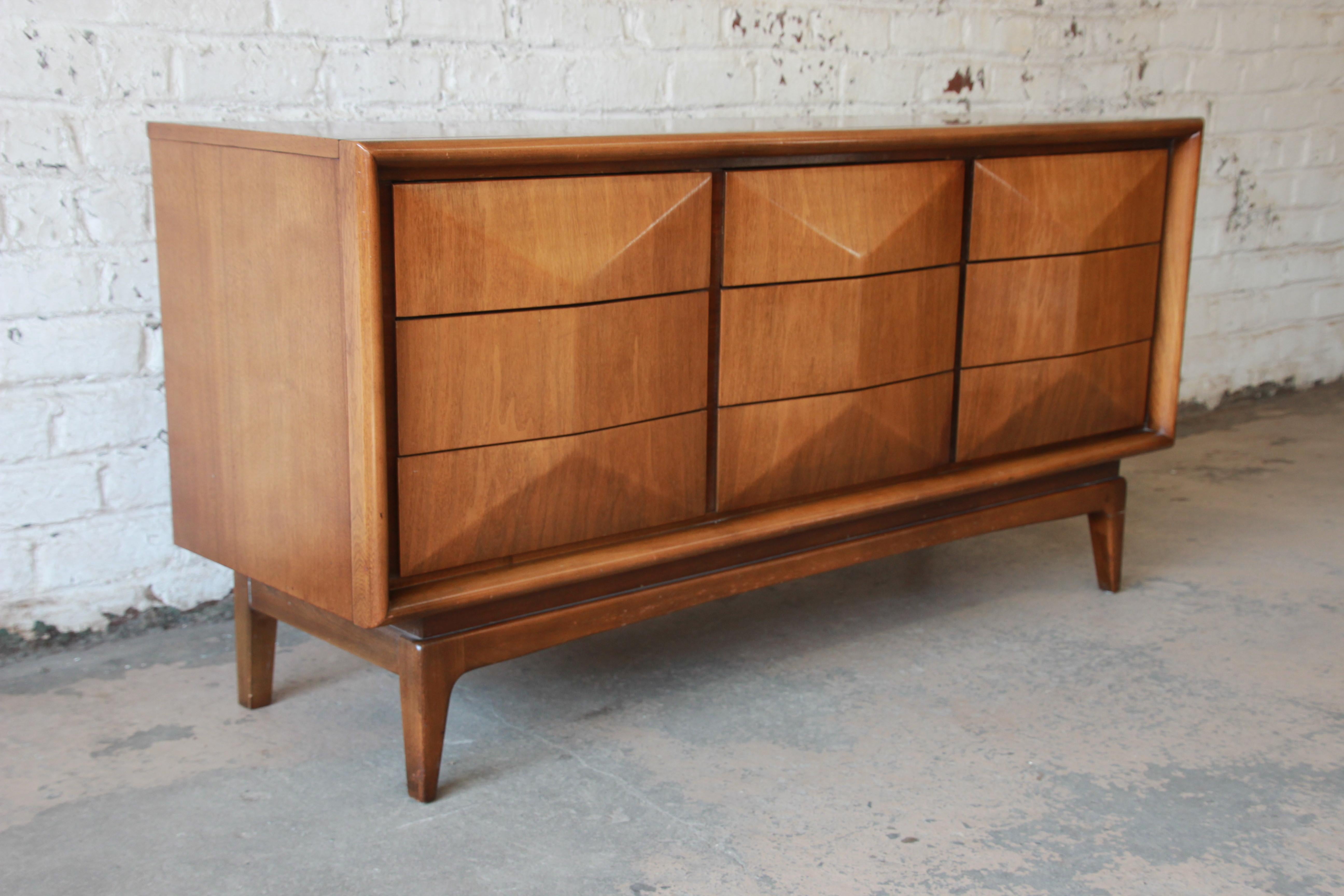 An exceptional and unique Mid-Century Modern diamond front dresser or credenza by United Furniture. The dresser features stunning walnut wood grain and a sculpted diamond front. It offers ample room for storage, with nine deep drawers. The dresser