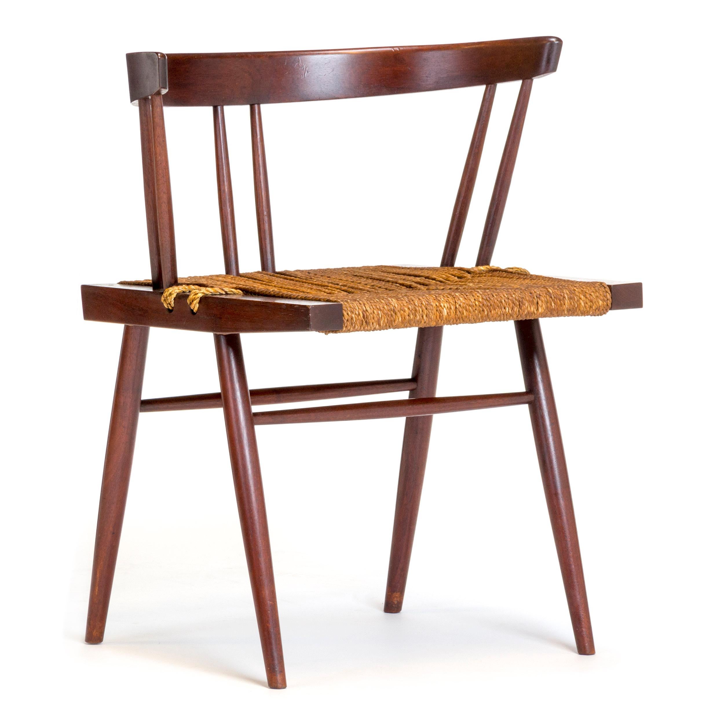 A walnut dining chair or side chair by leading American Craftman designer George Nakashima. Crafted by the George Nakashima Studio from solid walnut wood with a grass cord seat. Made in the USA. 

Also available in a lighter wood finish.