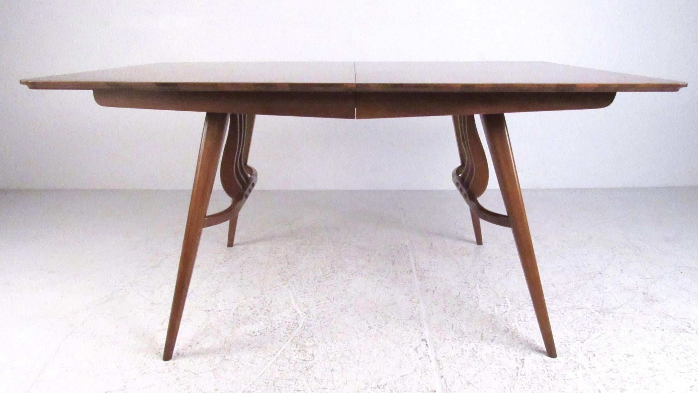 Cette élégante table de salle à manger moderne du milieu du siècle, fabriquée par Blowing Rock, est conçue en noyer et dotée d'une base décorative. Les pieds sont reliés par une barre transversale avec trois barres de support incurvées