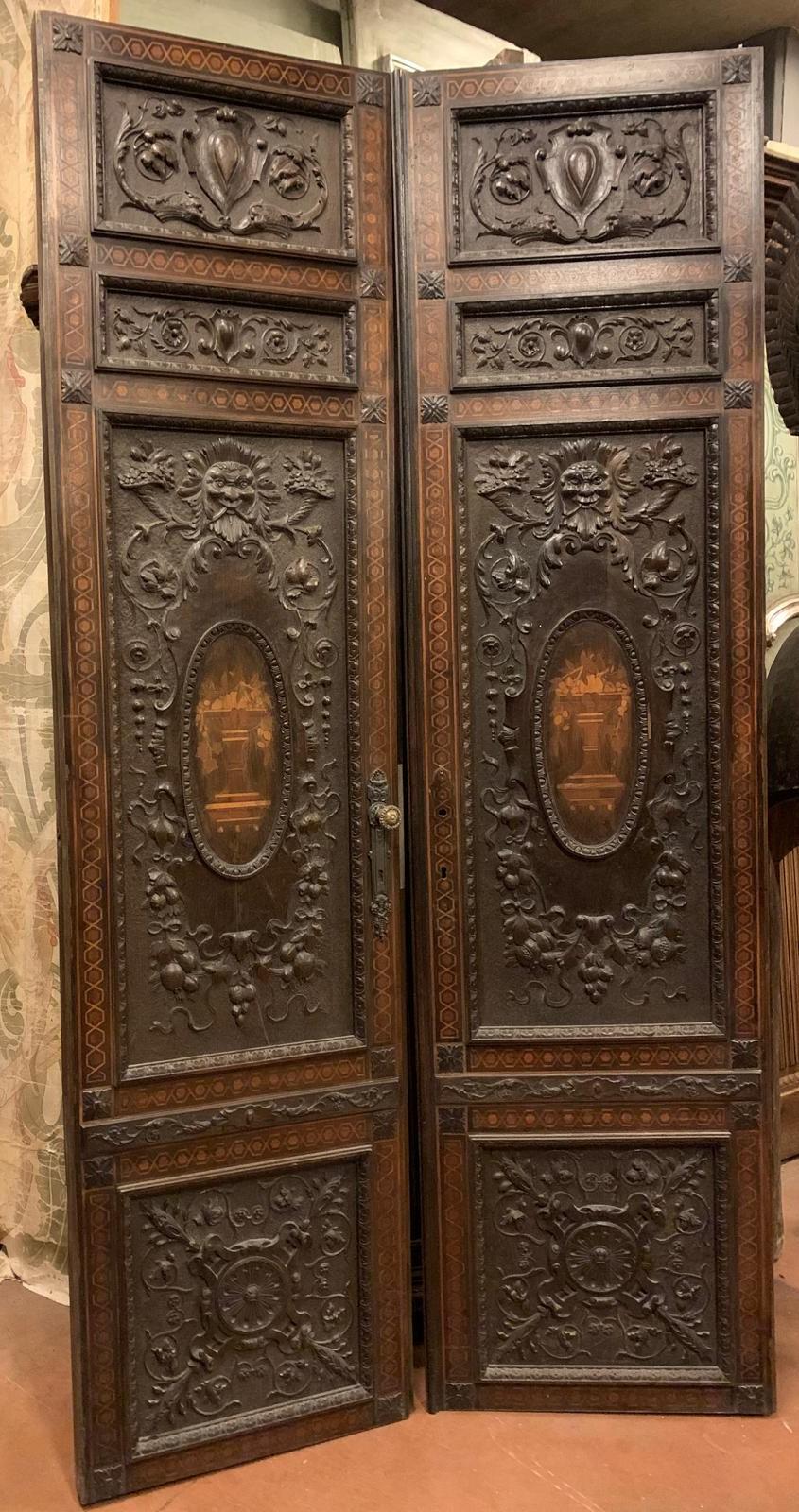 Porta antica per interni in noce massiccio, a due ante con pannelli riccamente intarsiati, intagliati con maschere, cornucopie e decorazioni floreali e fogliate.
Intarsiato con una coppa di frutta nell'ovale centrale, originale del XIX secolo,