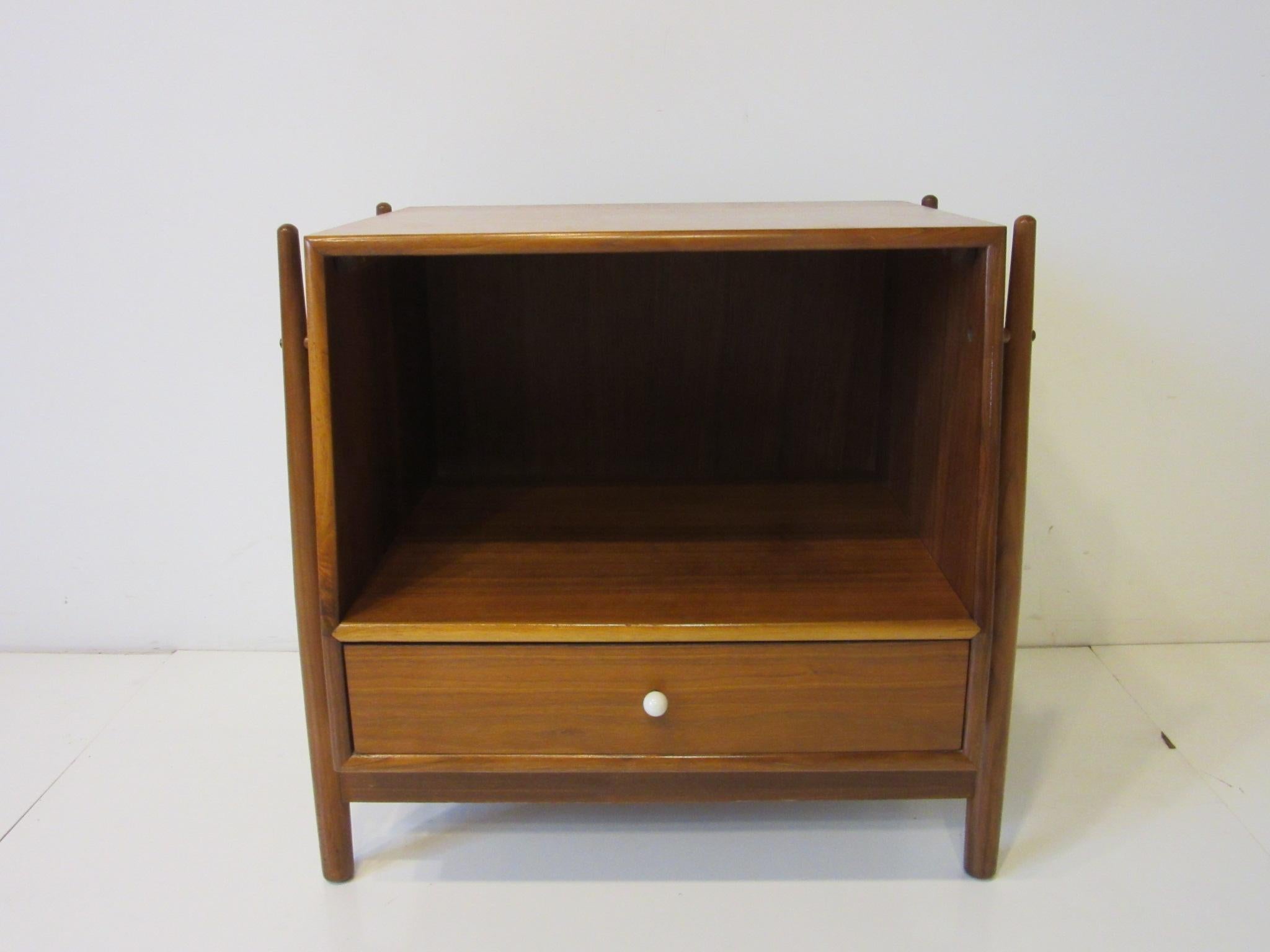 A well designed nightstand having one-drawer with a divider suspended on outer tapered legs and detailed with a white porcelain pull. The upper section offers storage, designed by Kipp Stewart for the Drexel Furniture company for their Declaration
