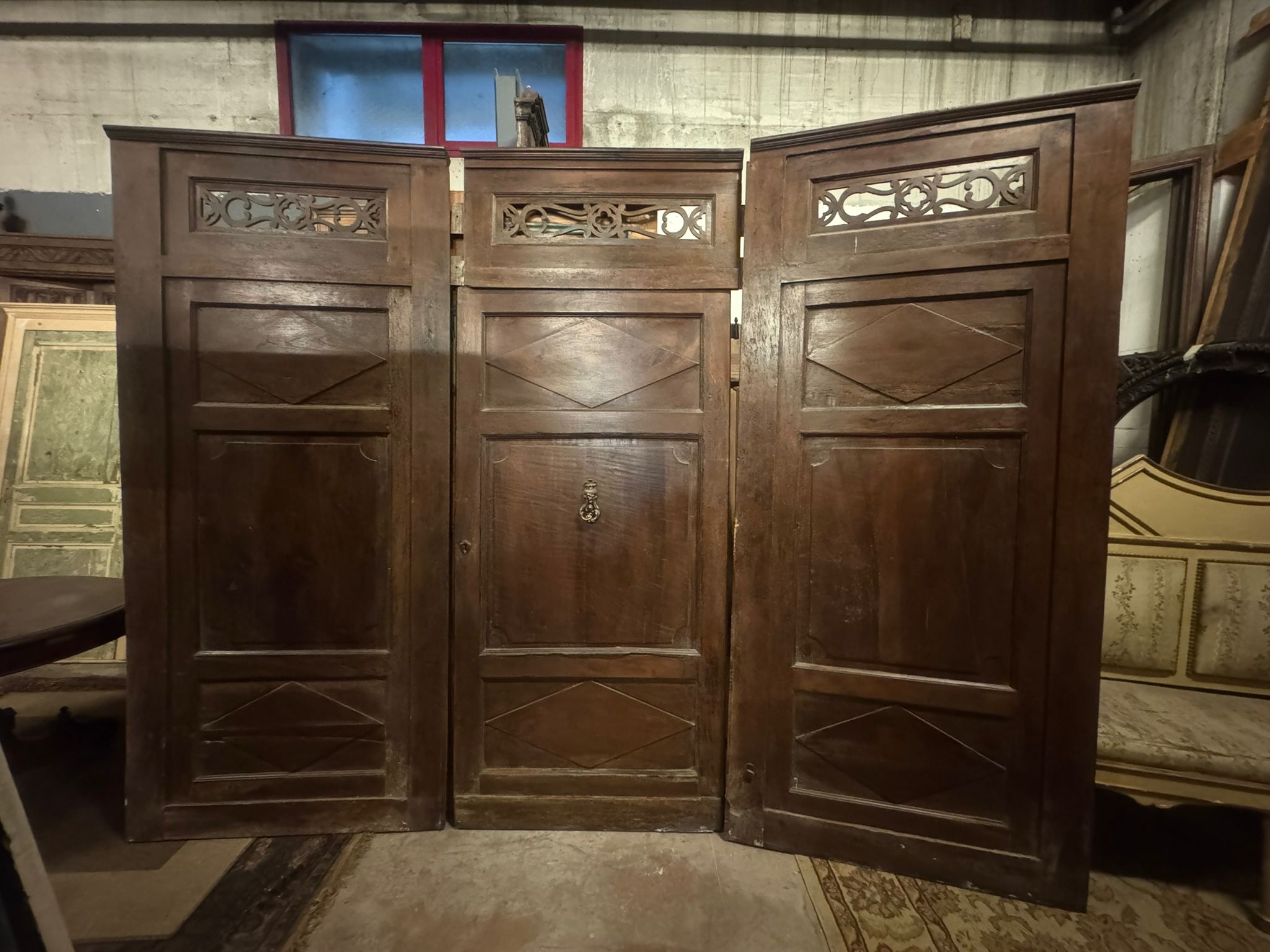 Antique entrance door, main door in solid walnut, composed of three doors with carved panels and central knocker in patinated iron. Complete with antique key, It has a double-sided central door with interlocking overdoor. Original from the 19th