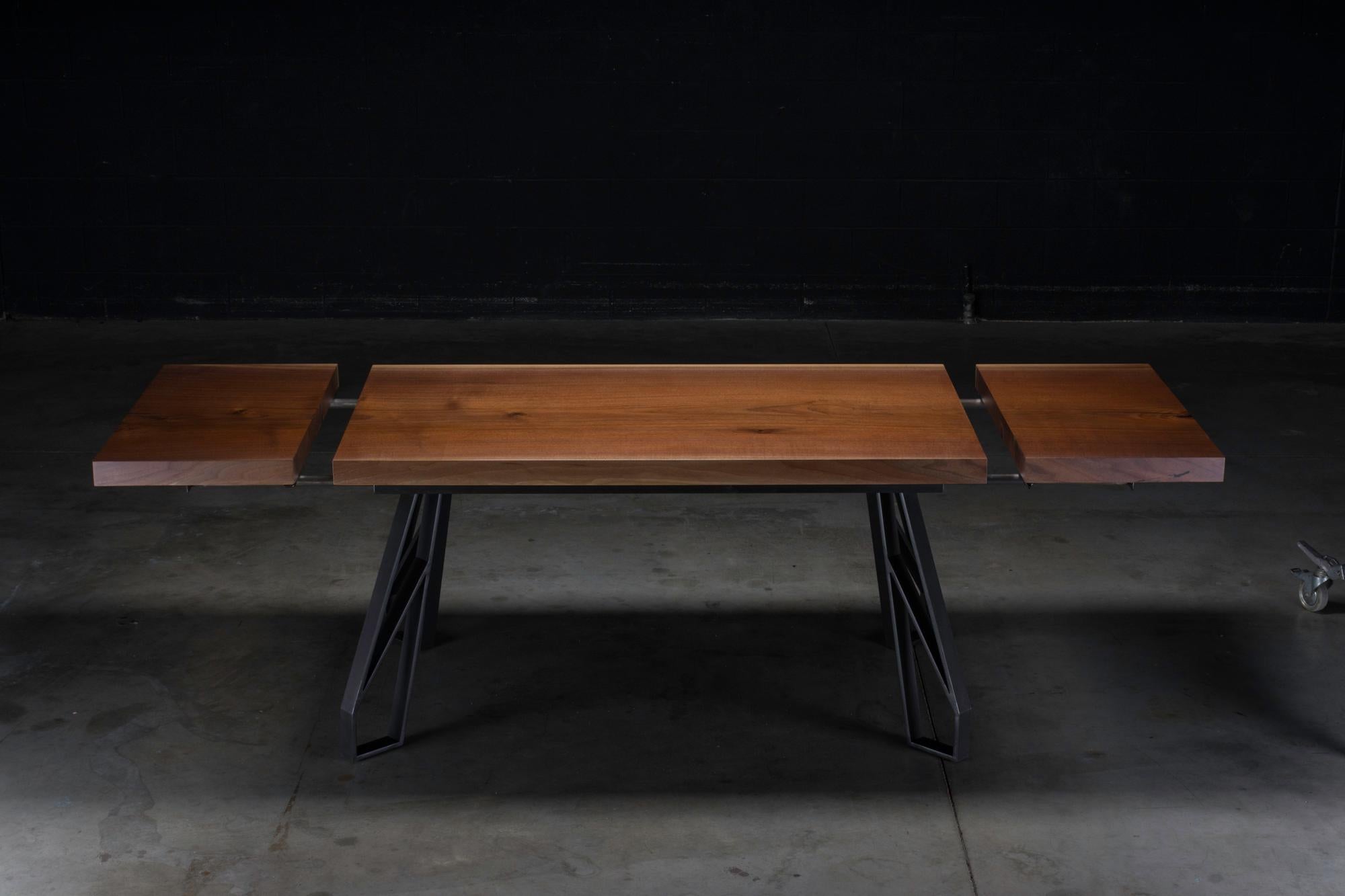 La table de salle à manger Chalmers est composée d'un plateau en noyer massif et de ferrures expansibles fabriquées à la main. Le plateau est posé sur des pieds en acier au design géométrique moderne. Cette table est suffisamment polyvalente pour