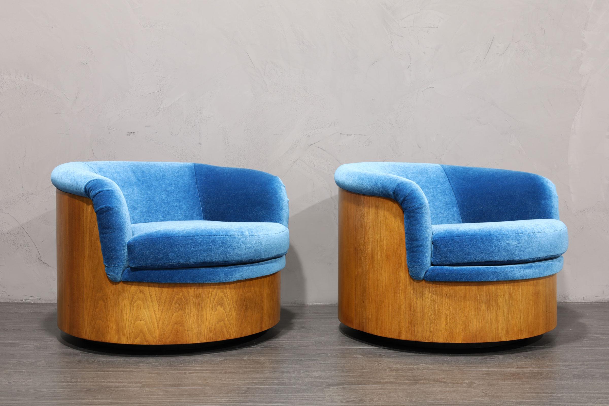 A very unique pair of swivel chairs attributed to Plycraft. These have a walnut veneer finish along the back and base. We have reupholstered in a blue mohair. The chairs are very comfortable and great looking!
