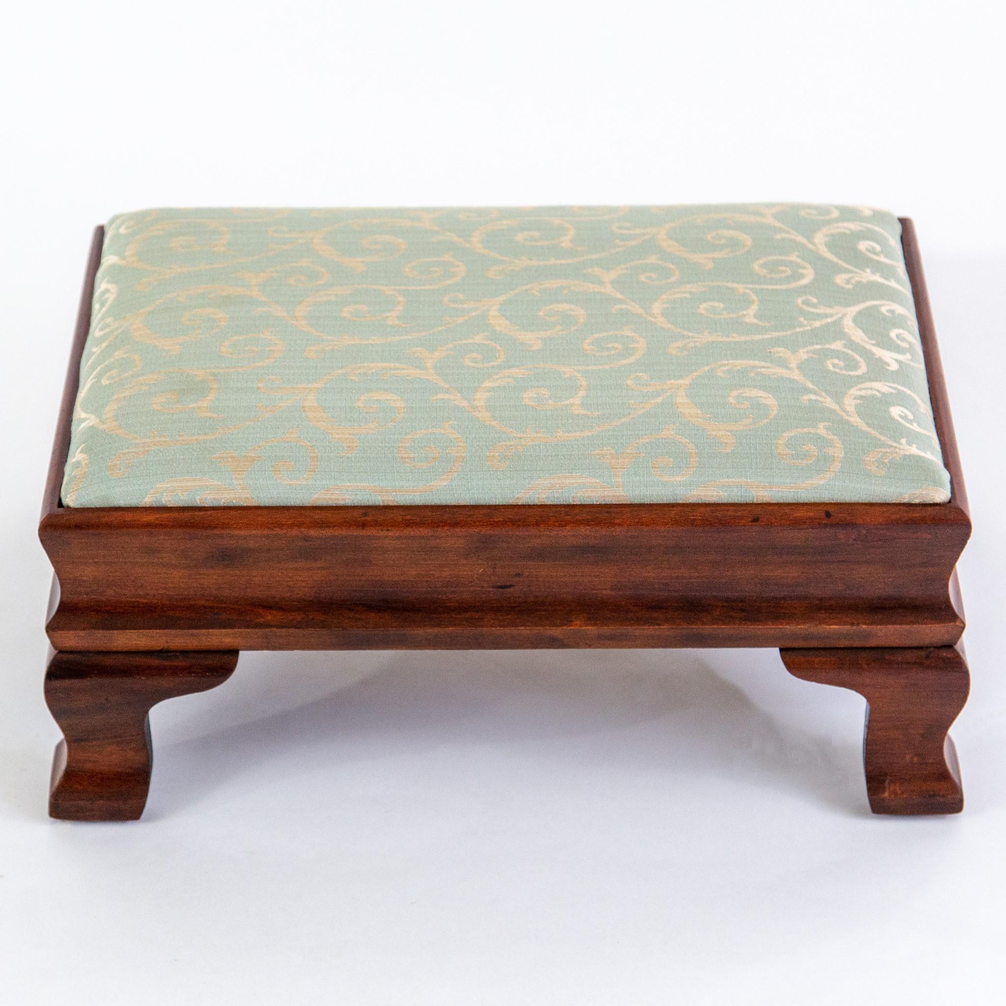 Mid-20th century American Colonial-style walnut footstool with ogee curved sides and bracket feet. The padded drop-in top is covered in light jade green fabric with a champagne scroll pattern. Very good vintage condition with minor age wear.