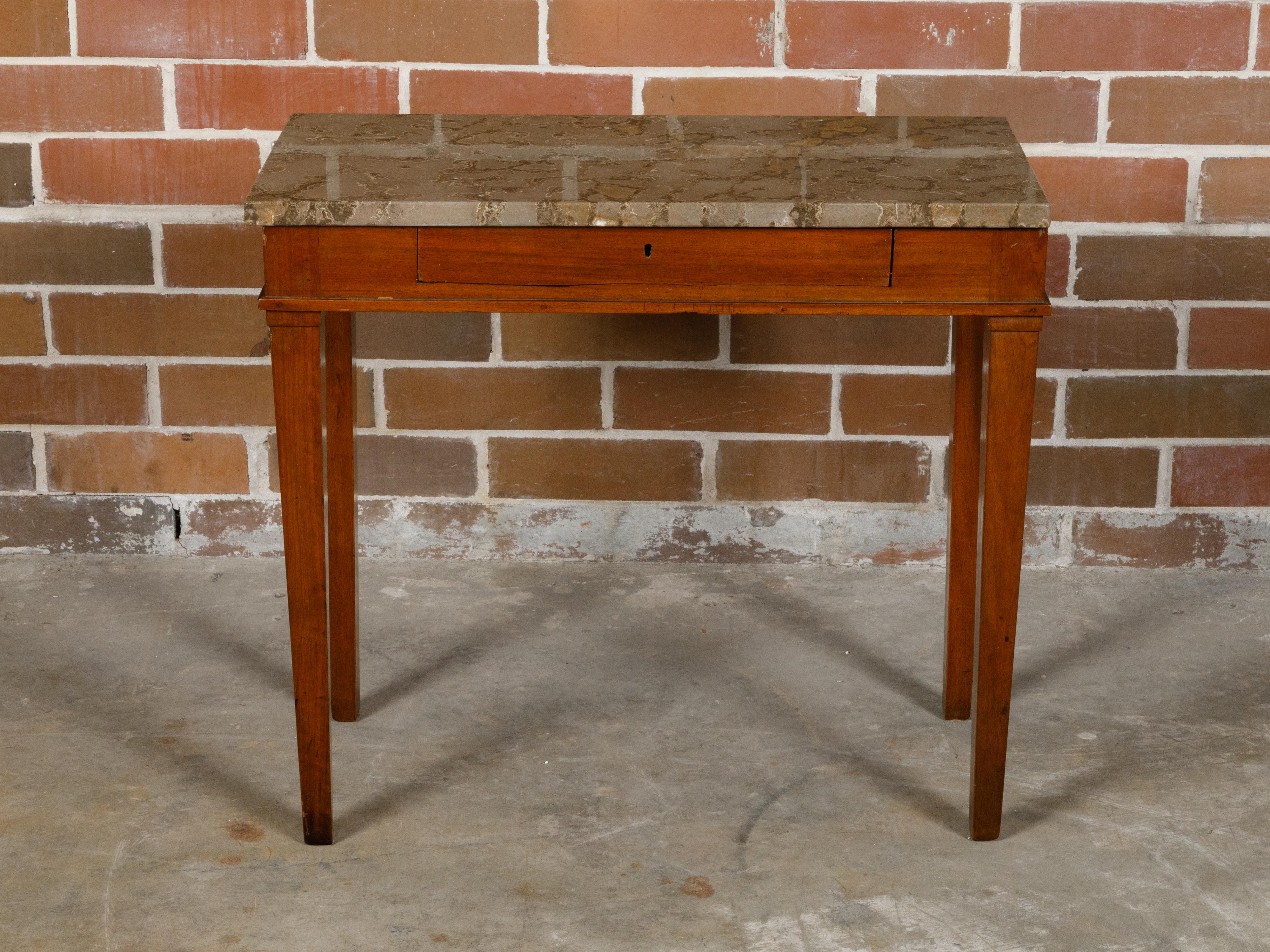 A French walnut console table from the 19th century with rectangular variegated marble top, single drawer and tapered legs. This French walnut console table from the 19th century is a piece of timeless elegance, seamlessly blending classic design