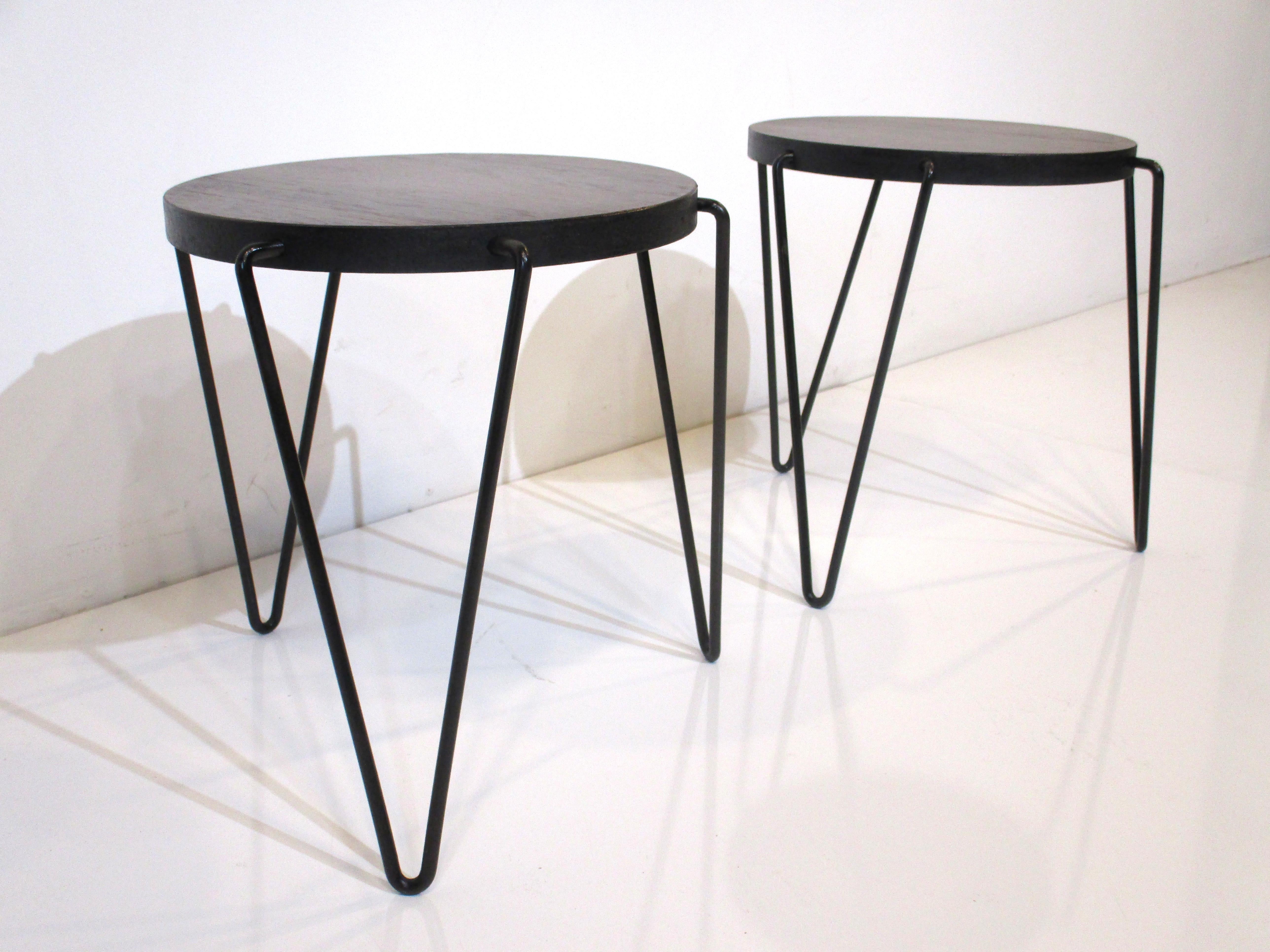 A pair of dark walnut topped round side tables with black edging and iron hairpin legs intergraded into the side of the table tops. This shows the extra design effort in making a clean interesting detail, having a partial label to the bottom from