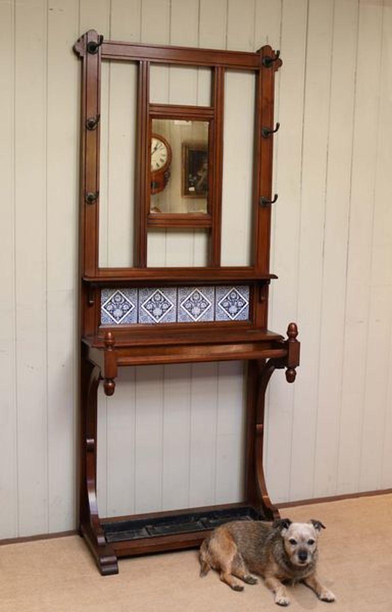 Walnut hall stand having a central rectangular mirror with an arrangement of six coathooks above a row of period blue and white tiles having a lift up glove box and stick/umbrella Stand to the base with turned finials and the original drip tray.
