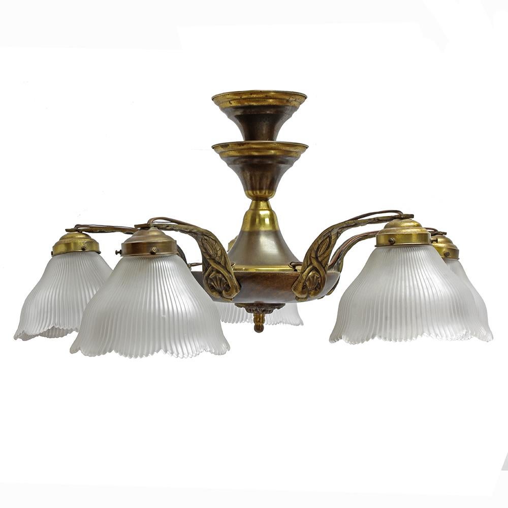 Epitomizing a 1920s modern aesthetic, this chandelier has sinuous lines, wood accents, and a beautiful silhouette. The walnut pan body of this fixture is fitted with brass accents, including the five arms each capped with a holophane shade. Put it